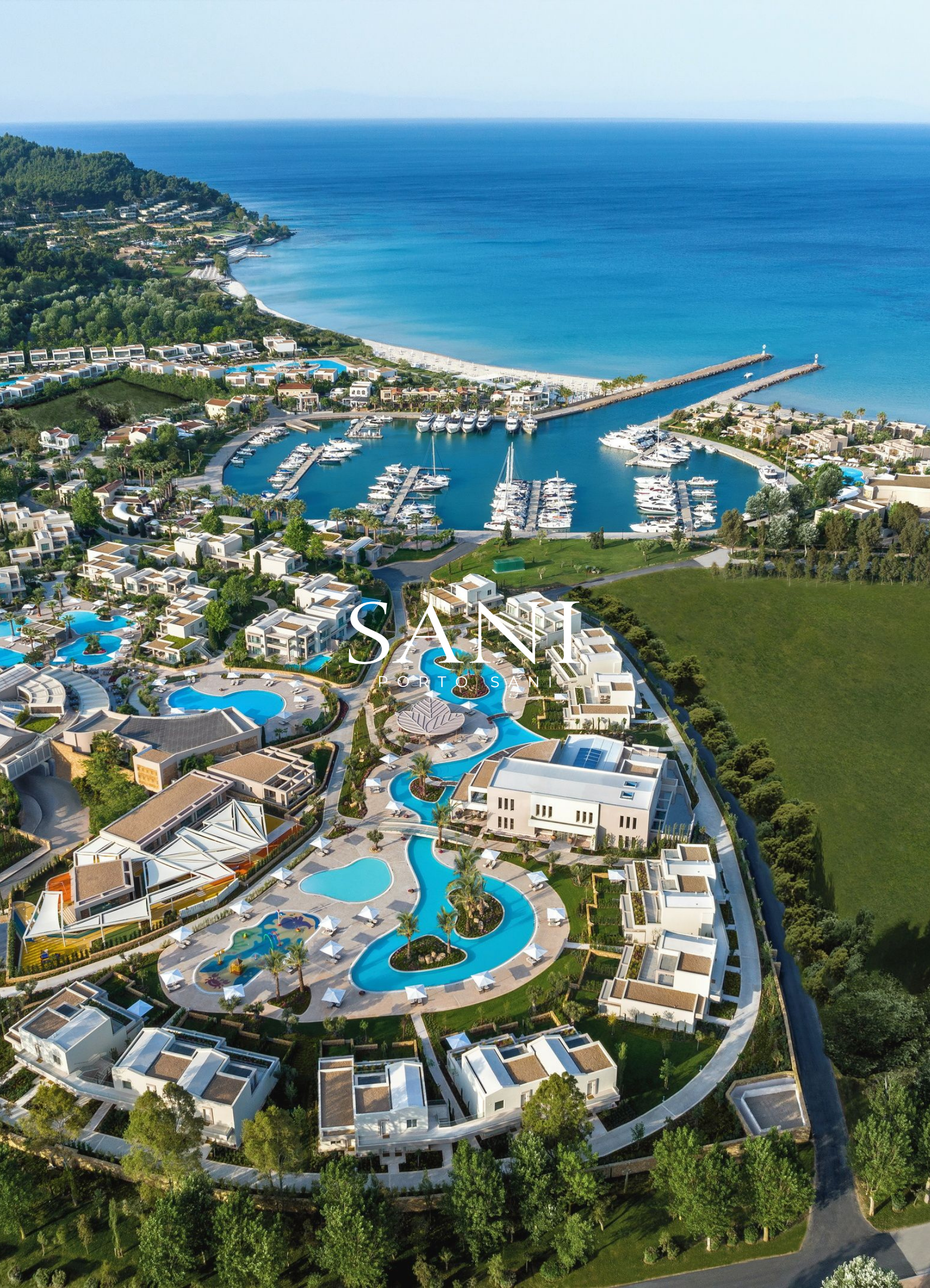 Aerial view of a coastal resort with swimming pools, marina with yachts, luxury villas, lush greenery, and the ocean in the background.