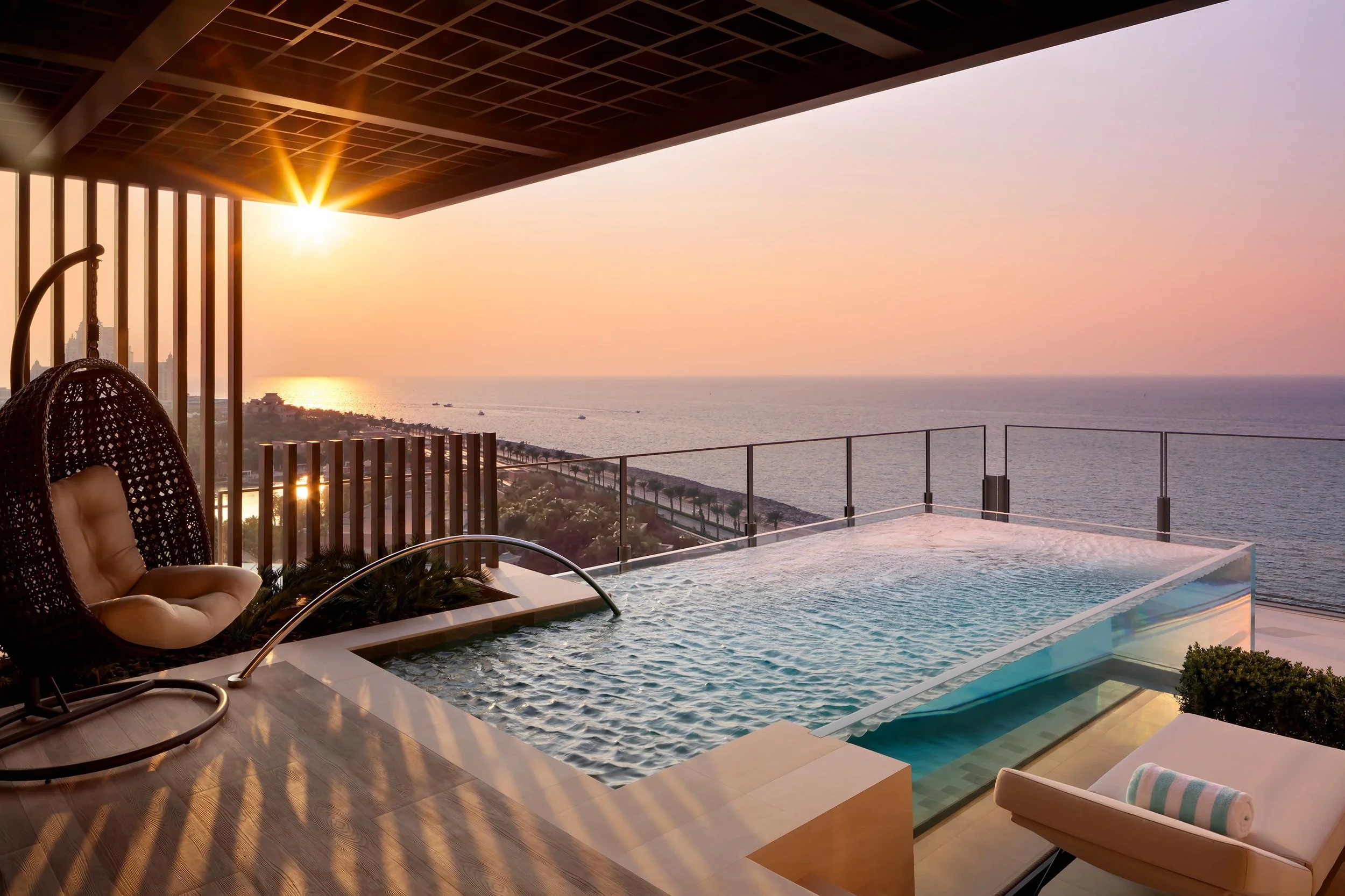 Luxury hotel balcony with infinity pool overlooking ocean at sunset.