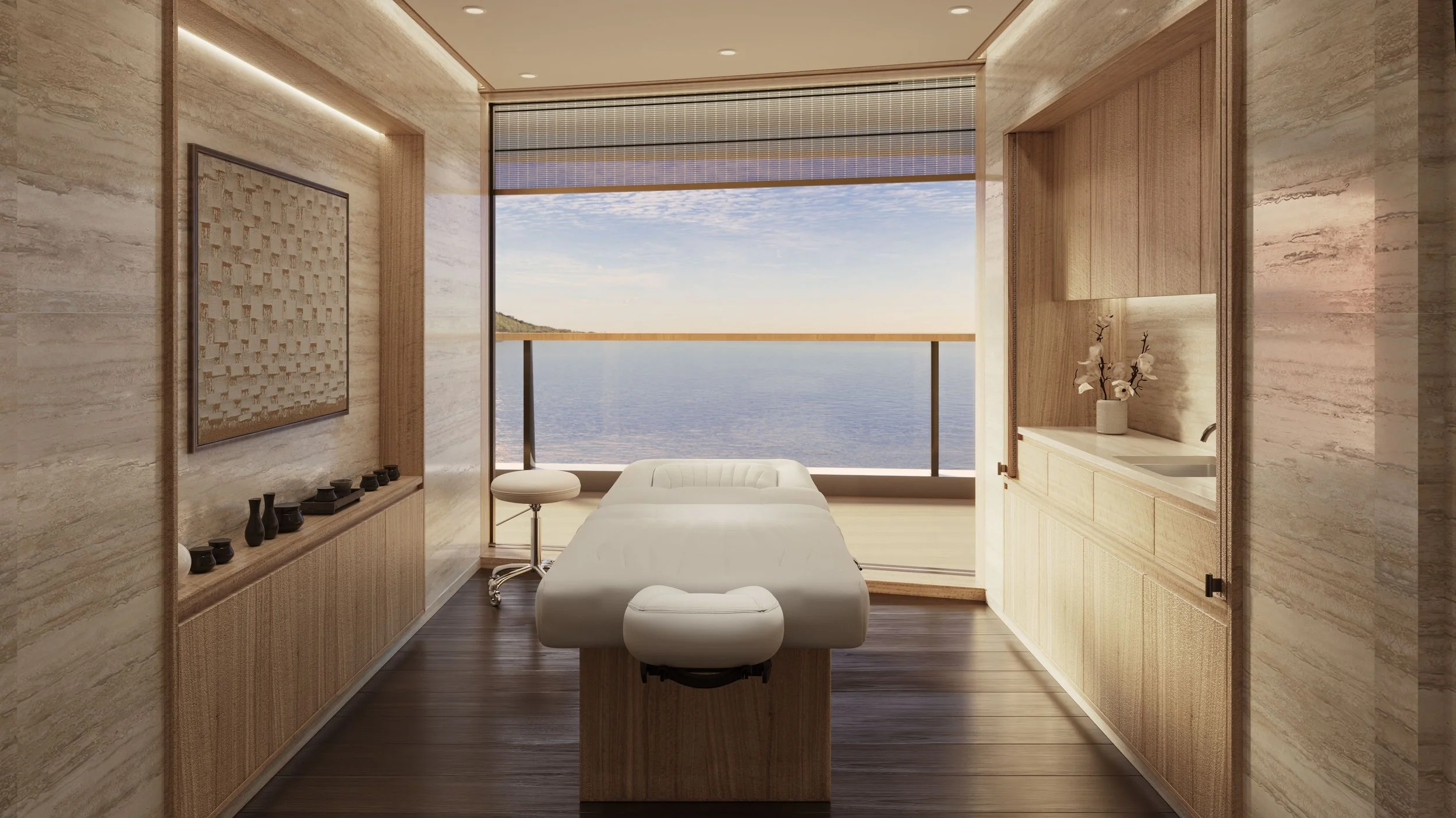 A modern spa room with a massage table facing large windows overlooking the ocean, decorated with a vase of white flowers and minimalistic furniture.