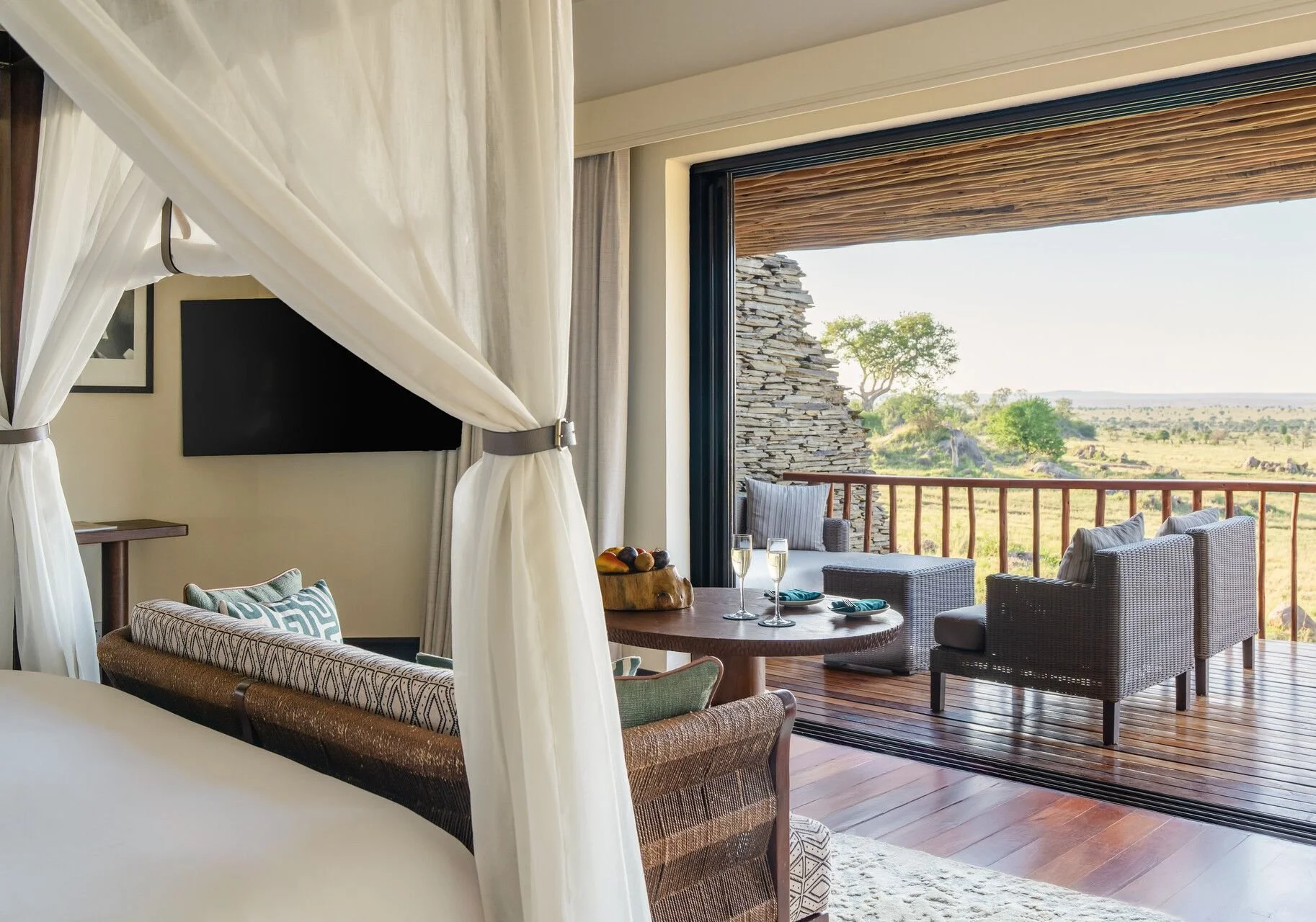 View of a cozy living room with a large open sliding door leading to a balcony with outdoor seating and scenic view of trees and savannah.