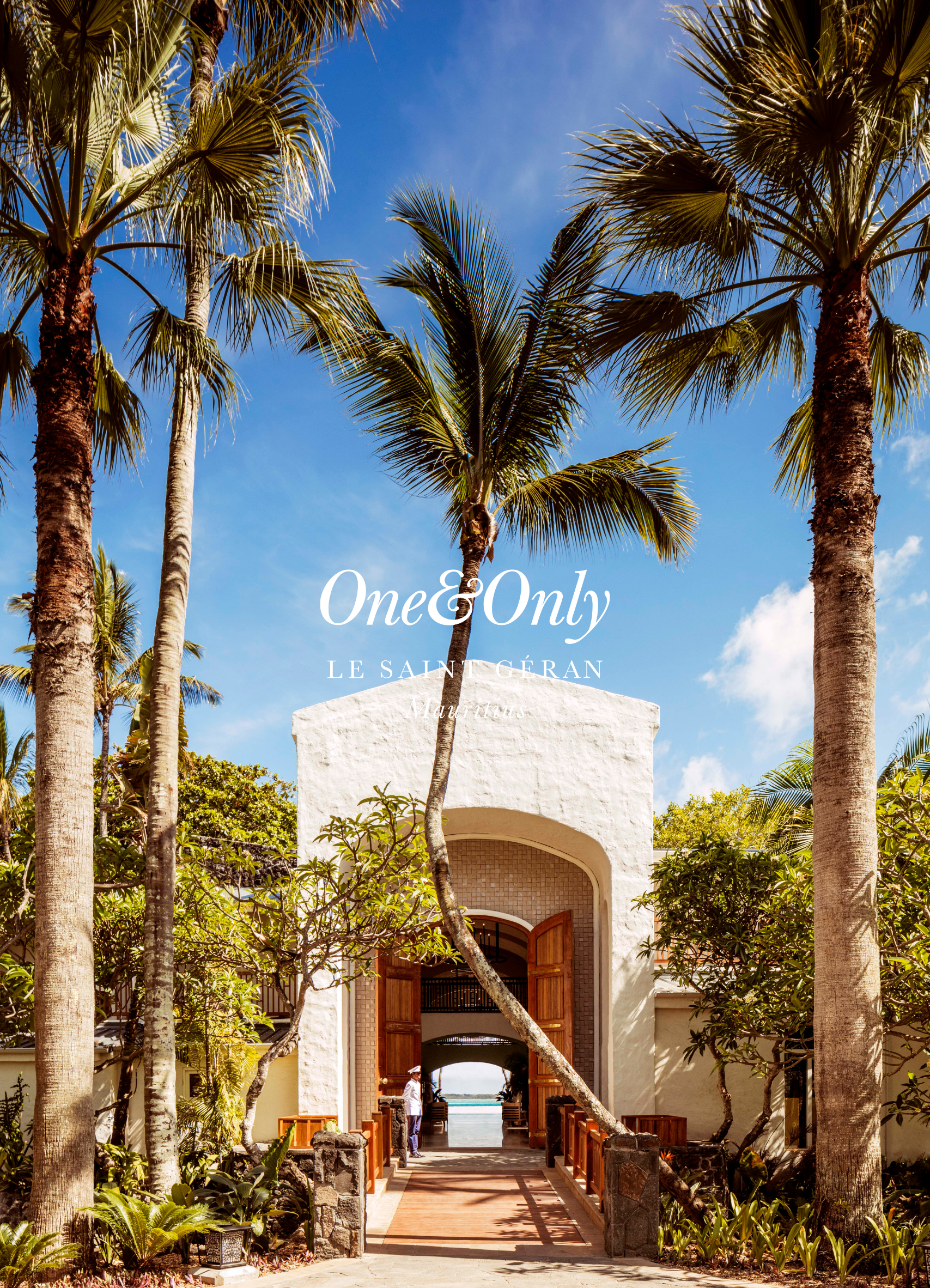 Beachfront archway with open wooden doors, surrounded by palm trees and tropical plants, leading to the ocean in the background.
