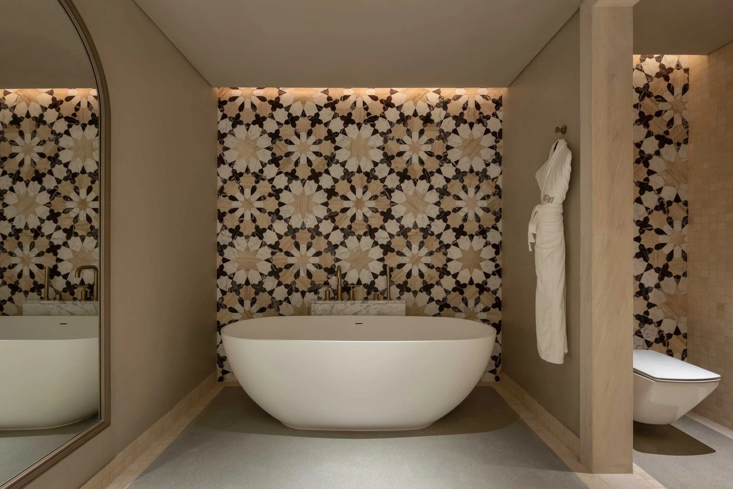 Modern bathroom with a freestanding bathtub, decorative tiled wall, toilet, and a mirror.