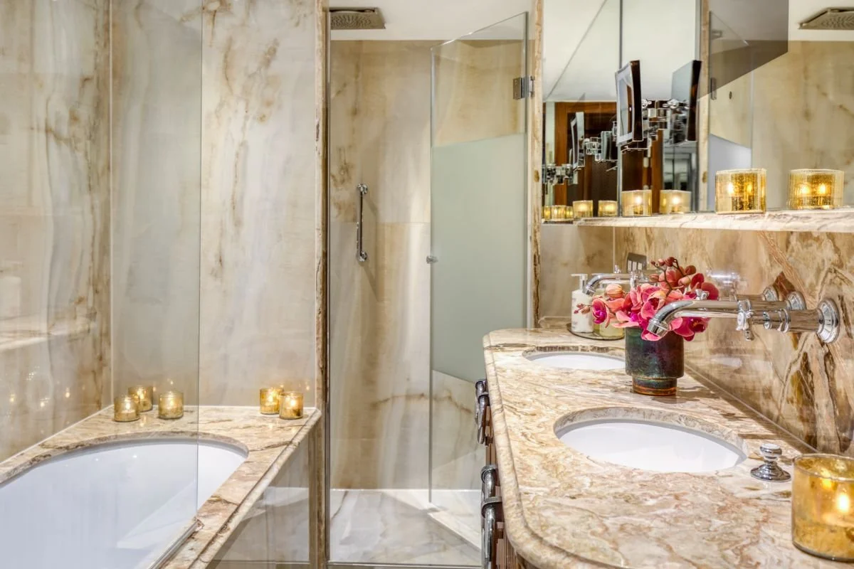 Bathroom with marble countertops, two sinks, a mirror, candles, and a flower arrangement.