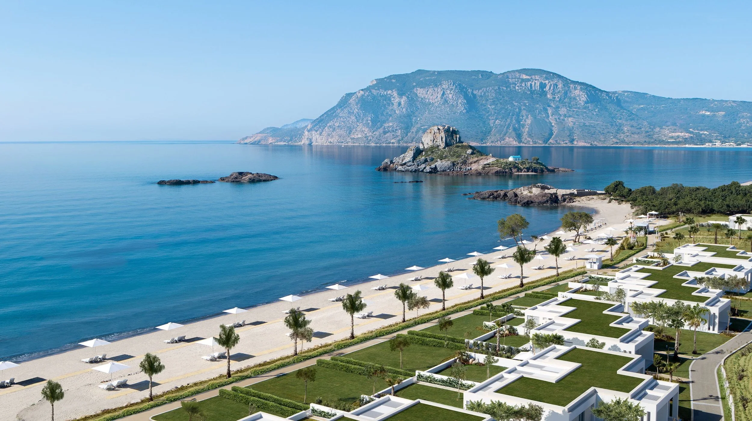 A coastal scene with a beach, white umbrellas, lounge chairs, palm trees, green lawns, and modern white buildings along the shoreline. In the background, there are rocky islands and a mountain.