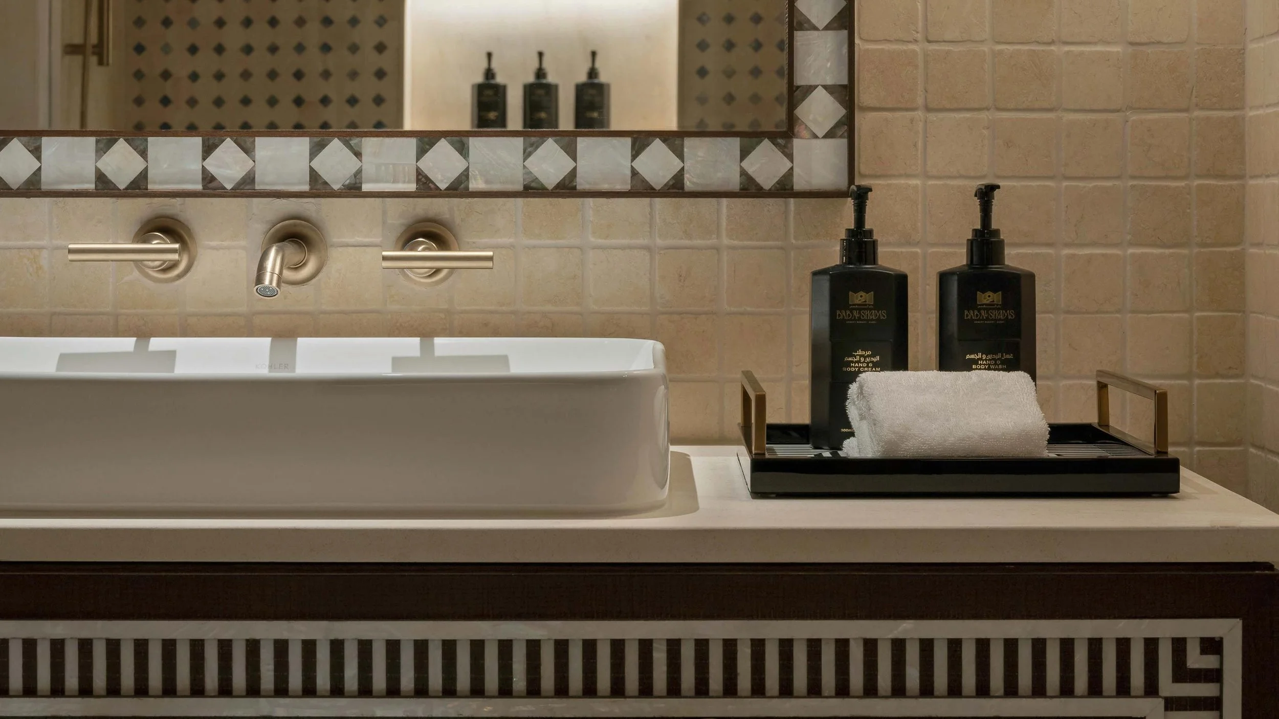 Bathroom countertop with a white sink, soap dispensers, and a tray with a towel and body wash bottles.