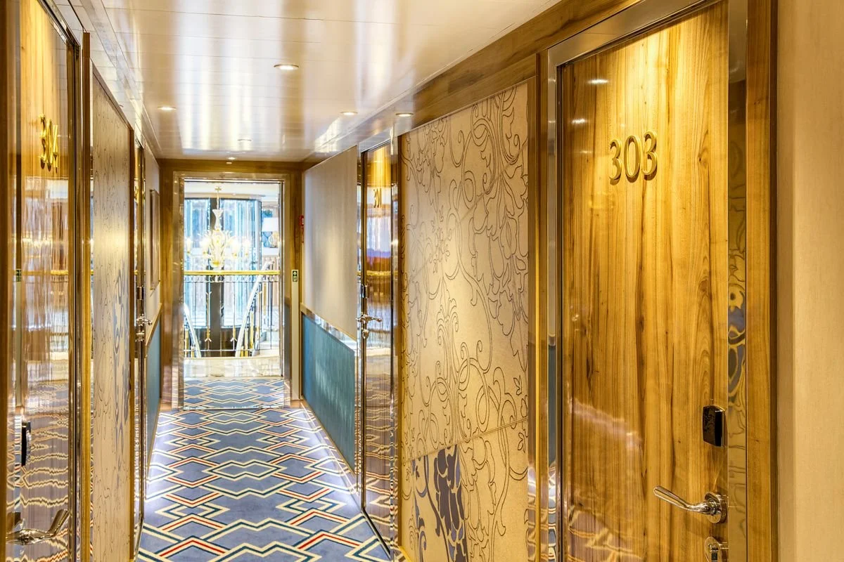 Hotel hallway with wooden doors, floor with geometric pattern, and gold-colored decorative panels.