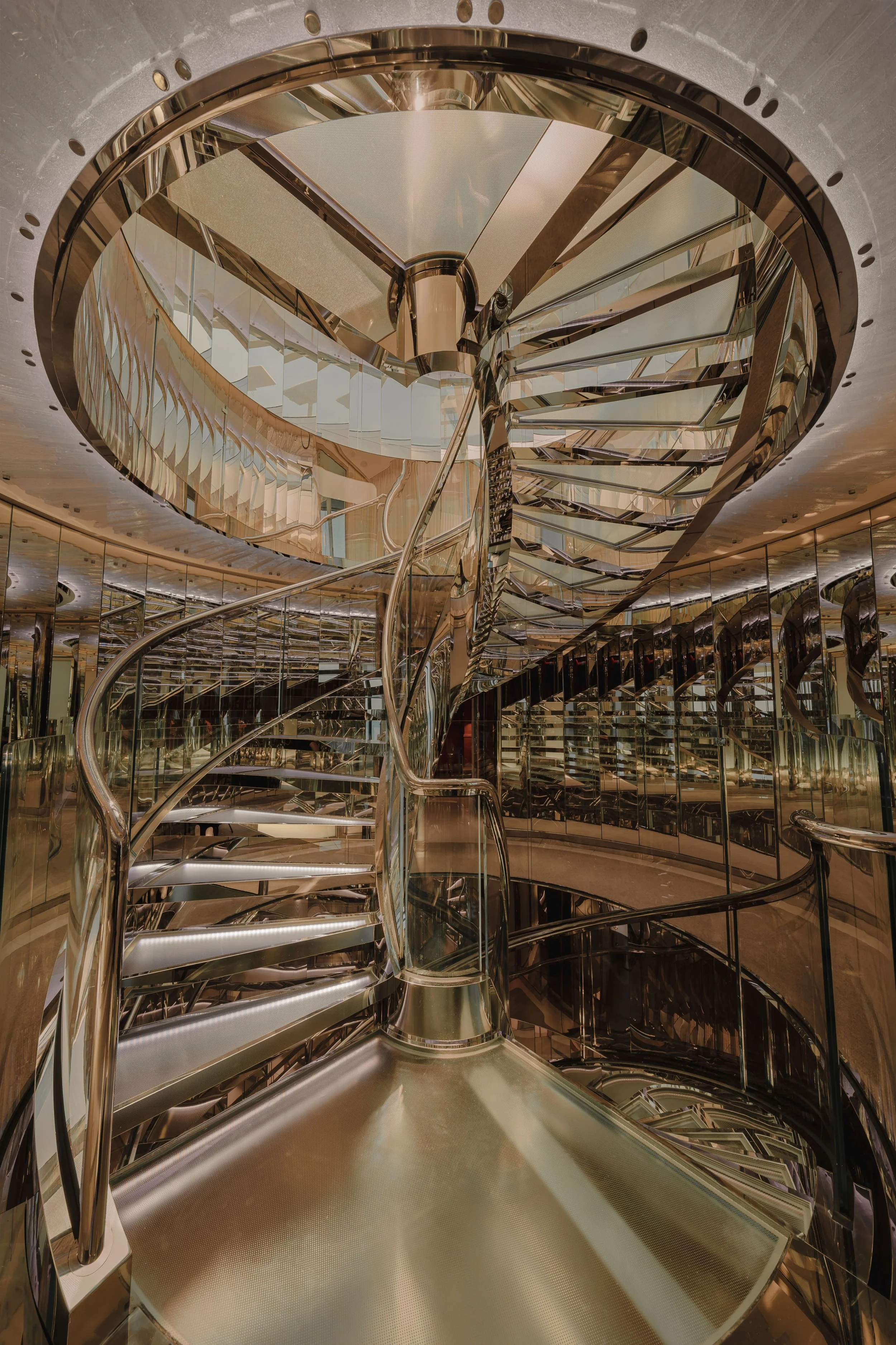Elegant spiral staircase with reflective gold and mirrored surfaces in a modern building interior.
