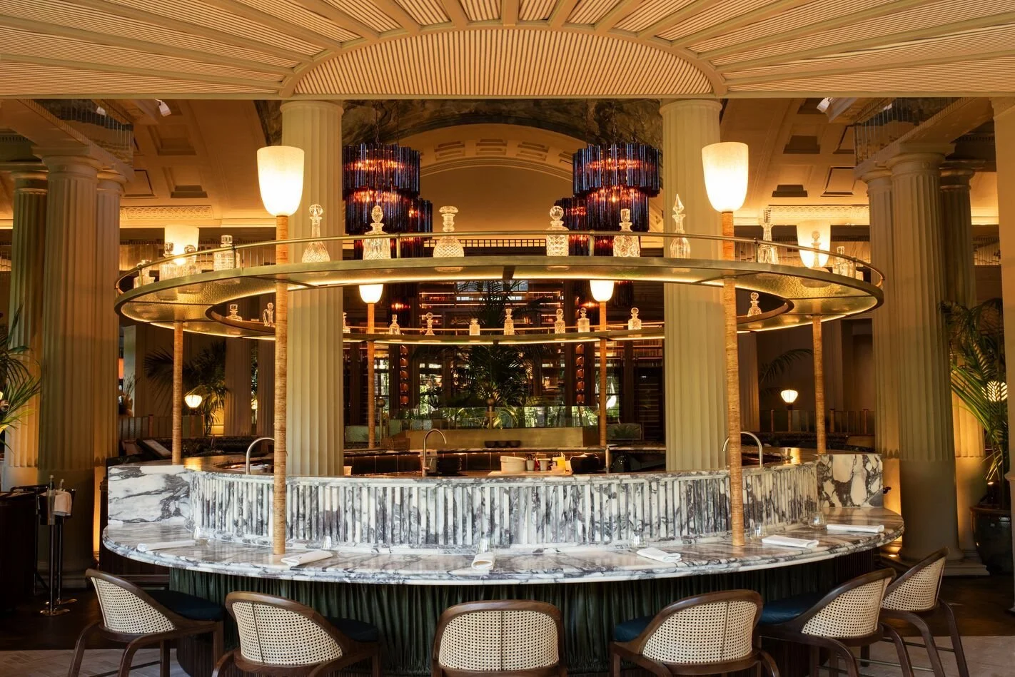 Luxurious restaurant bar with marble countertop, tall columns, modern lighting, and decorative bottles, featuring an elegant and inviting ambiance.