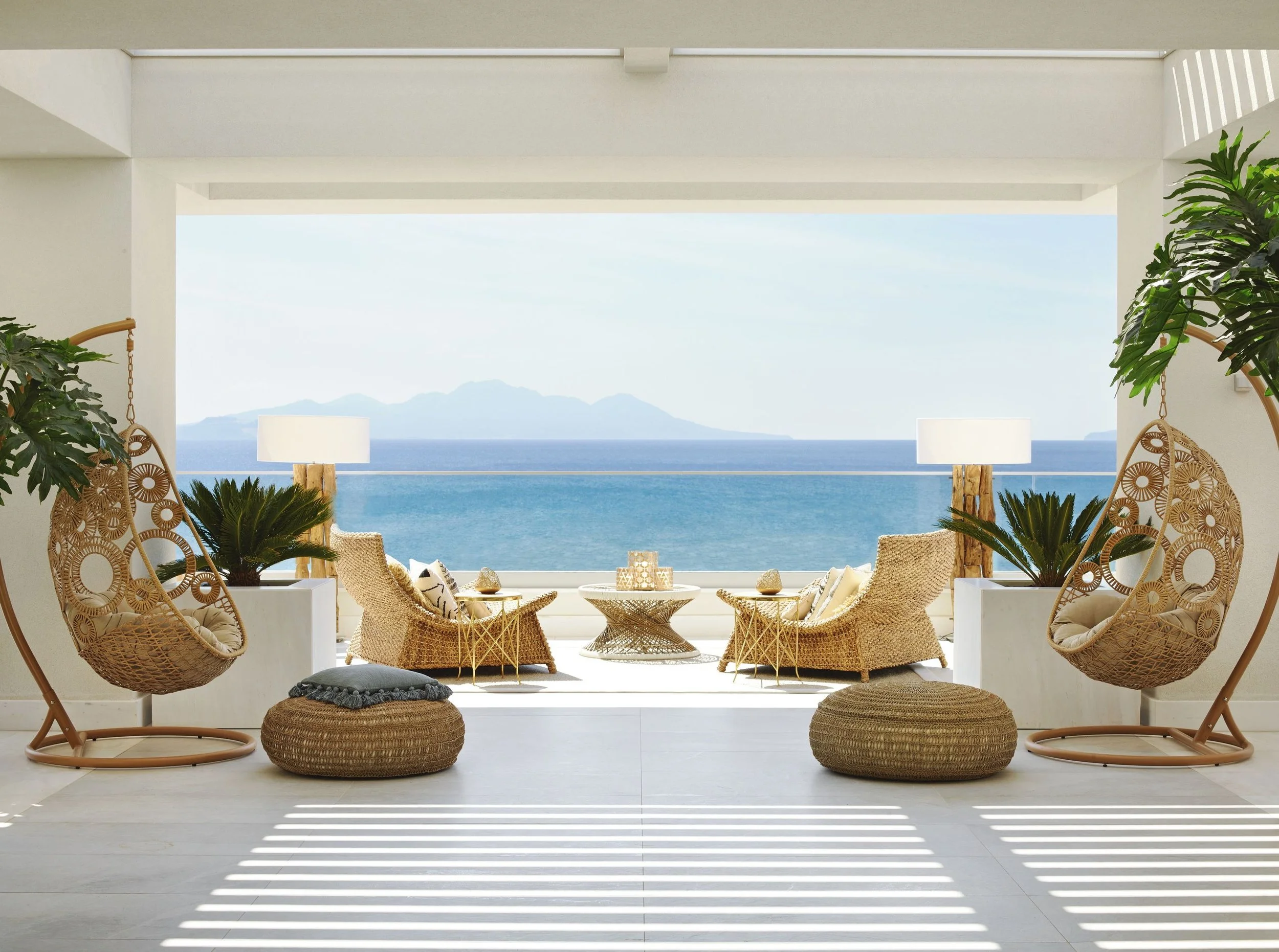 Living room overlooking ocean view with wicker chairs, plants, and patterned accents.