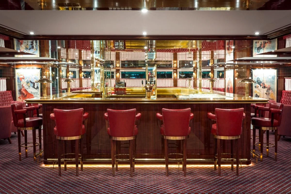 An elegant bar with a gold countertop, red leather bar stools, and mirrored walls in a luxurious setting.