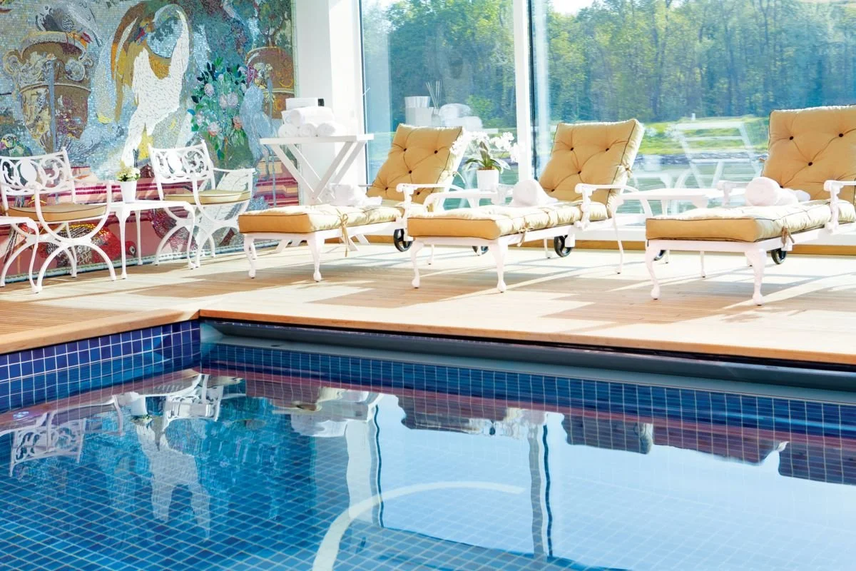 Indoor pool area with four yellow lounge chairs and a glass wall with greenery outside.