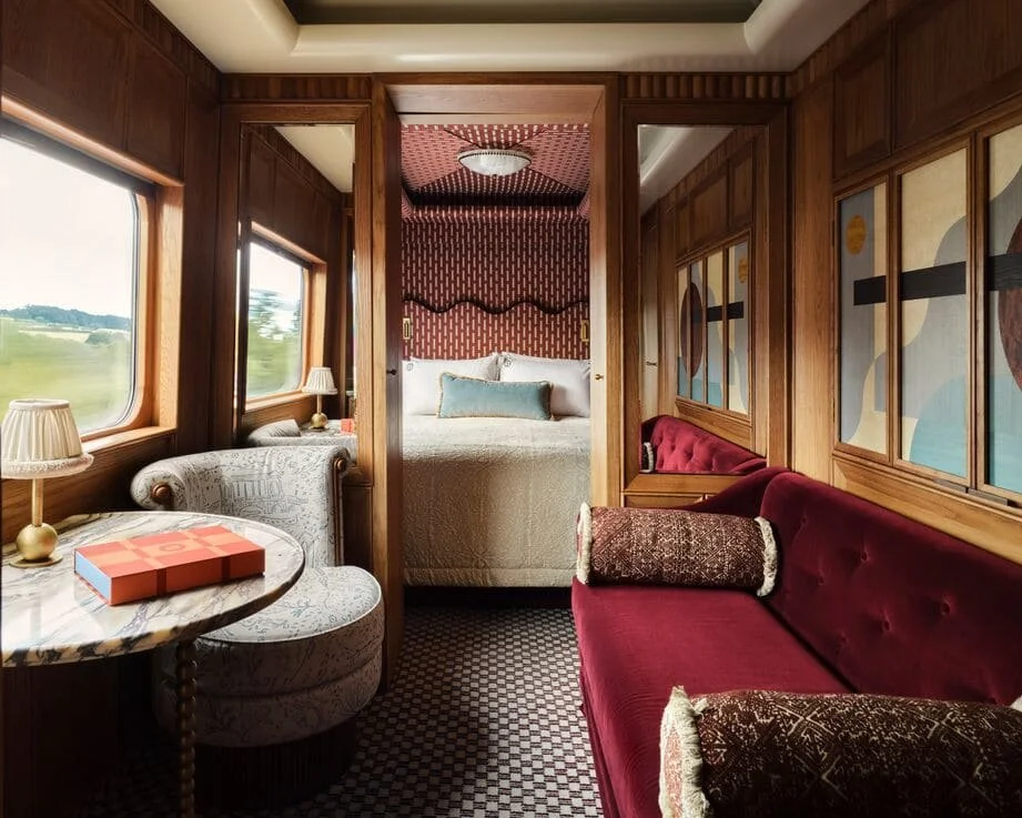 Interior of a cozy bedroom with wood paneling, a bed with a headboard and decorative pillows, and a sitting area with a red velvet sofa and a round marble table.