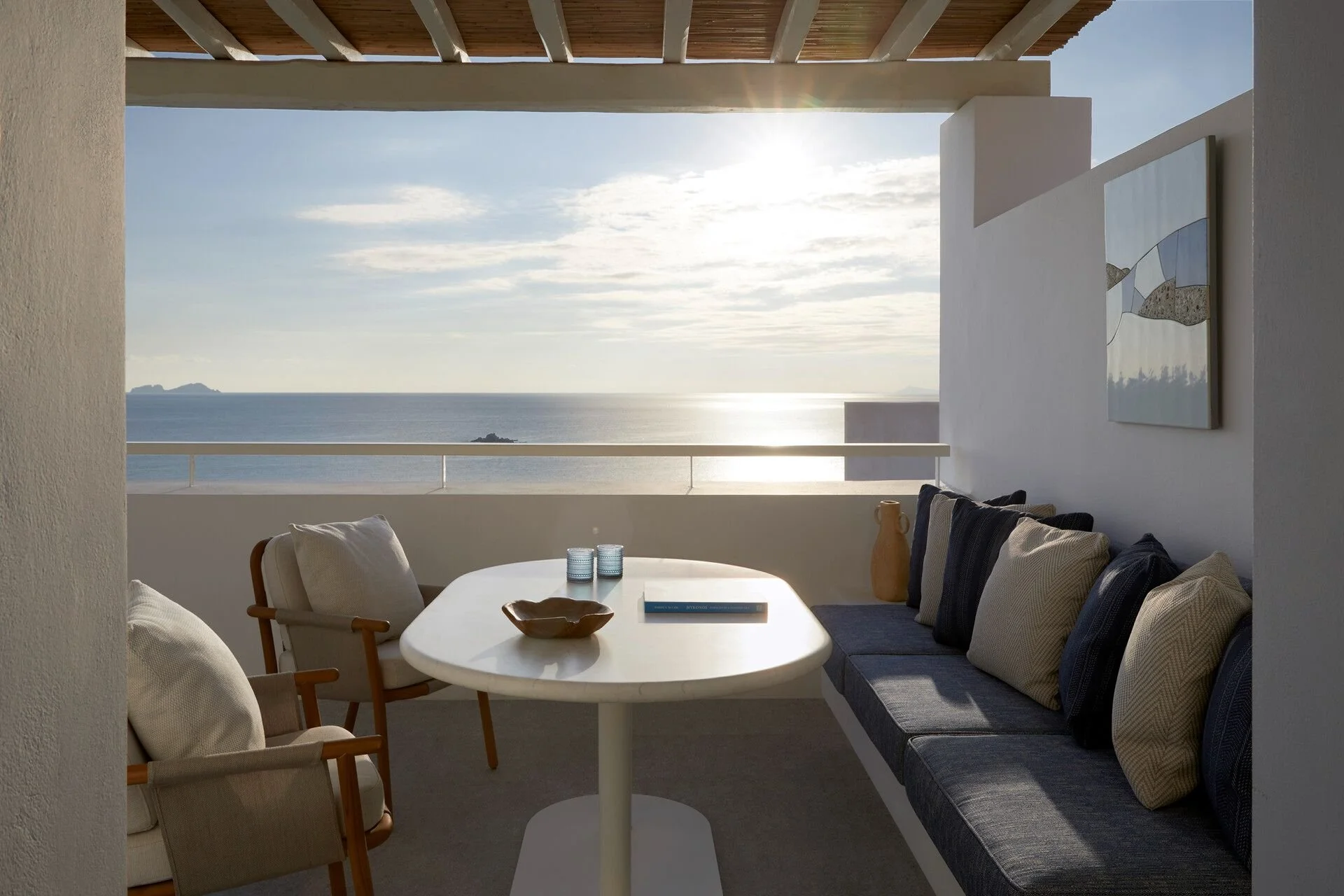 Image of a balcony with a white table and beige chairs, overlooking the ocean with the horizon and sky visible.
