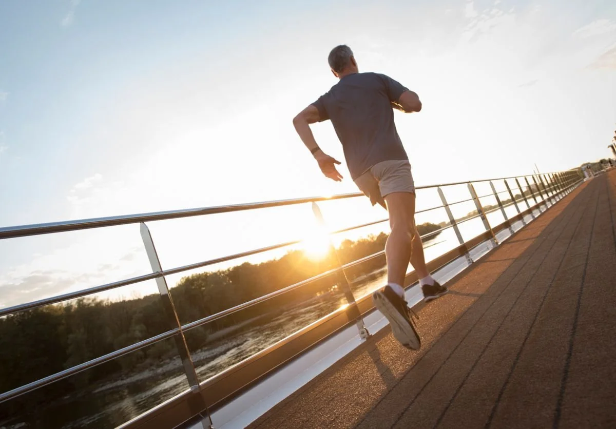 A man running on a bridge during sunset, with the river and trees visible in the background.