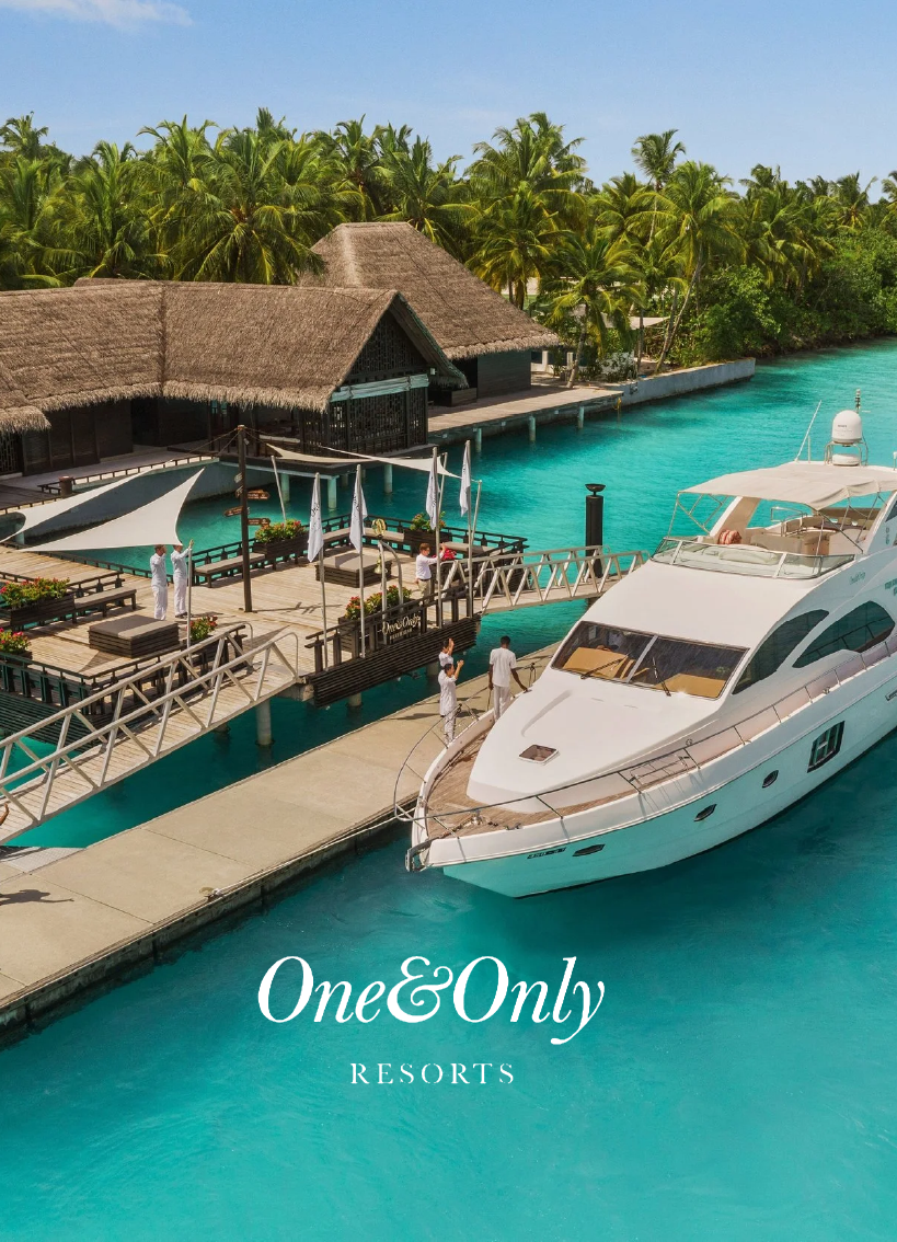 Luxury resort with overwater bungalows, a dock with a yacht, surrounded by tropical palm trees and clear blue water.