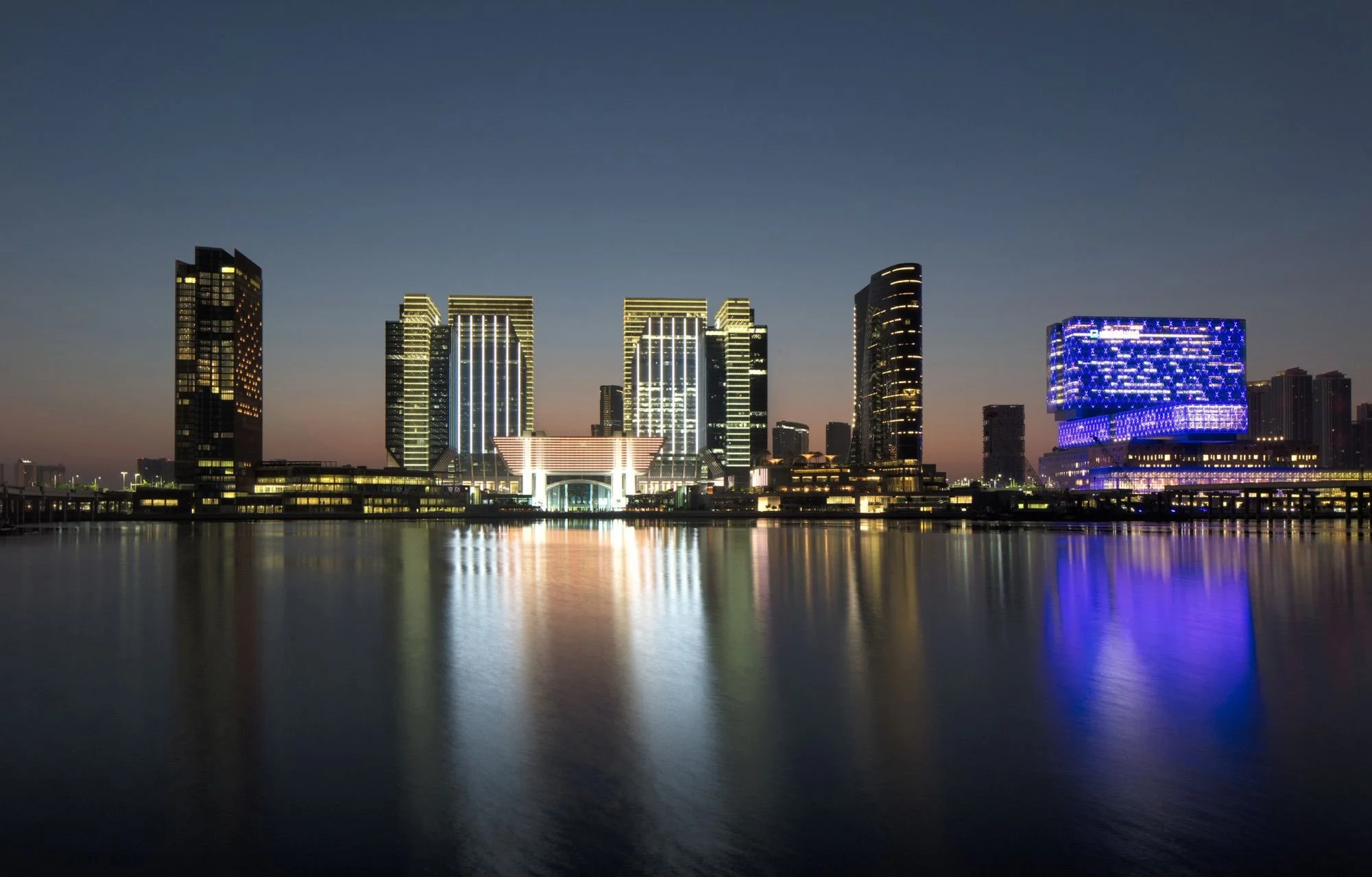 City skyline at night with illuminated modern skyscrapers and their reflections on the water.