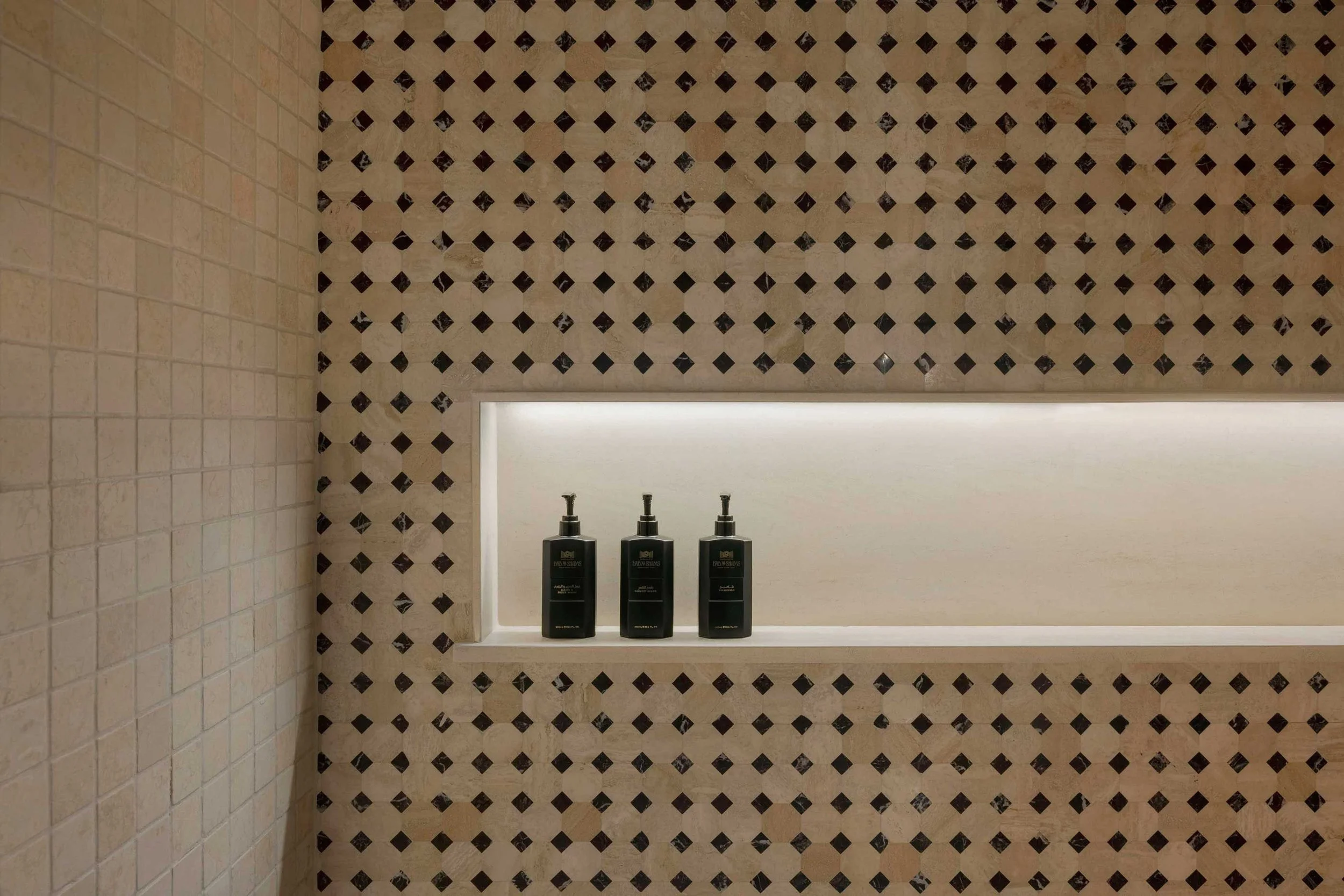 Bathroom with tiled walls, featuring a shelf with three black bottles labeled 'Moisturizing' and a mirror above.