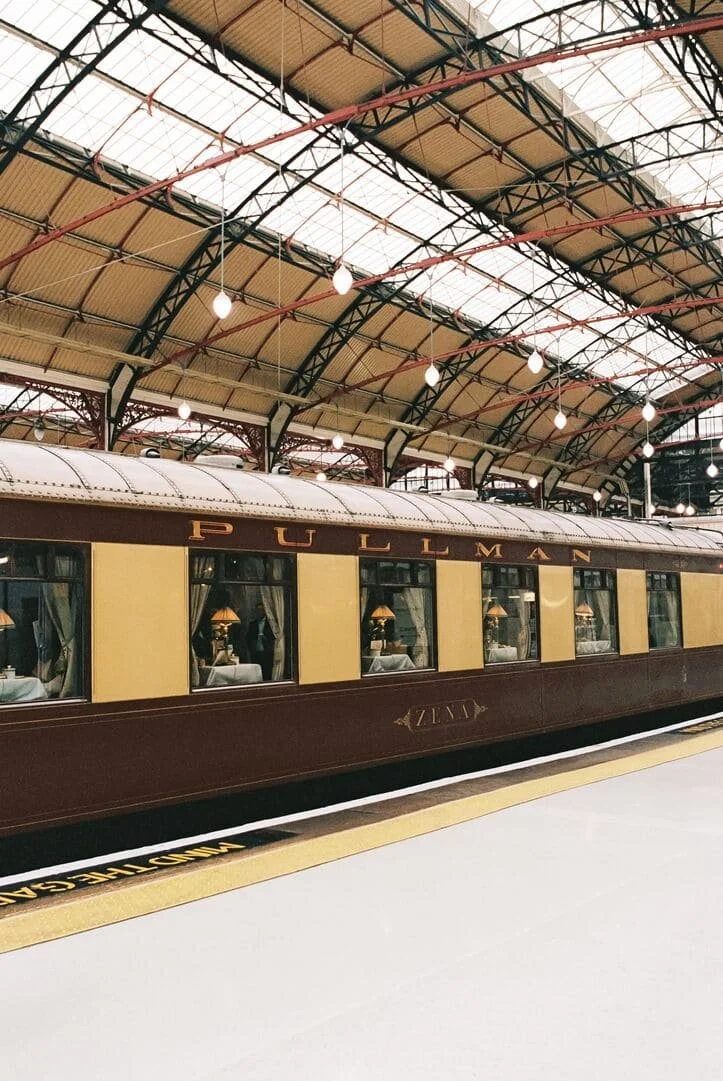 Vintage Pullman train car at a station with a high arched ceiling and hanging lights.