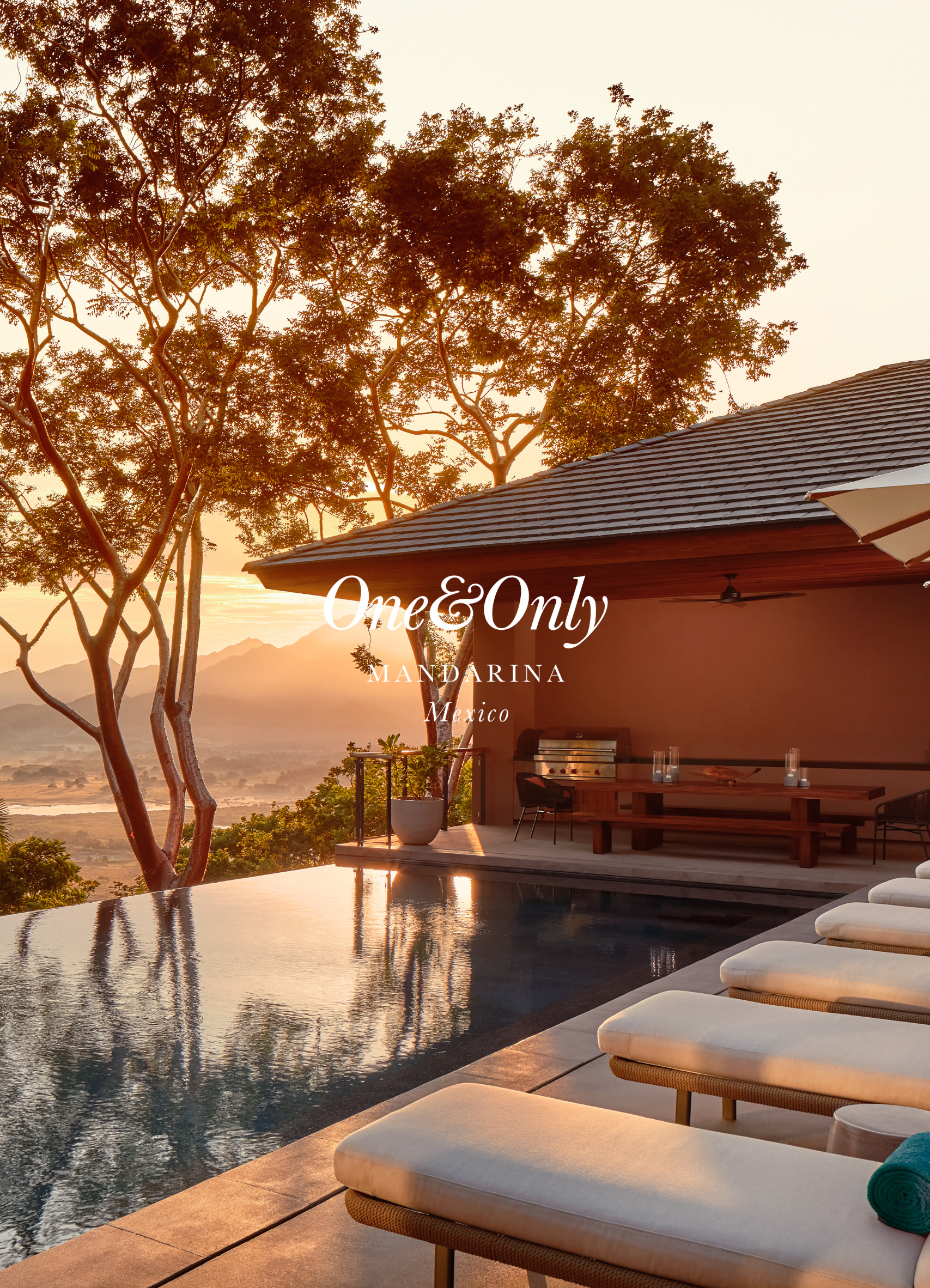 View of a deck with lounge chairs overlooking a swimming pool and tropical trees at sunset in Mandarina, Mexico.