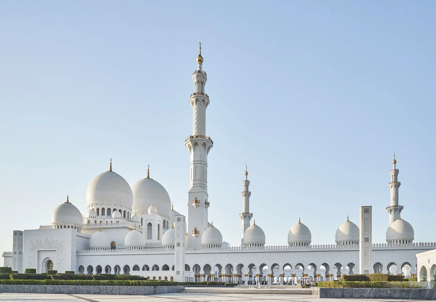 View of the Sheikh Zayed Grand Mosque in Abu Dhabi with white domes and minarets against a clear sky.