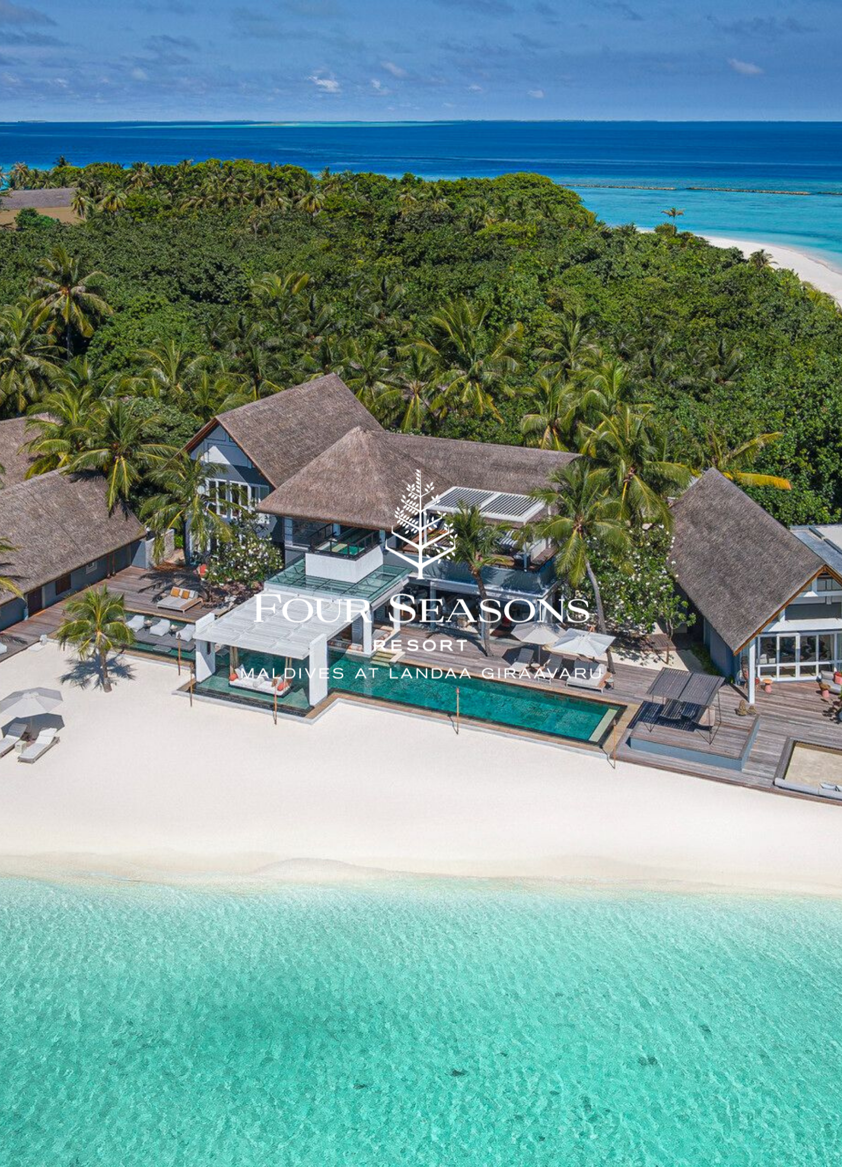 Aerial view of a resort with thatched roof buildings, a swimming pool, white sand beach, turquoise ocean, and lush green trees at Landa Giraavaru, Maldives.