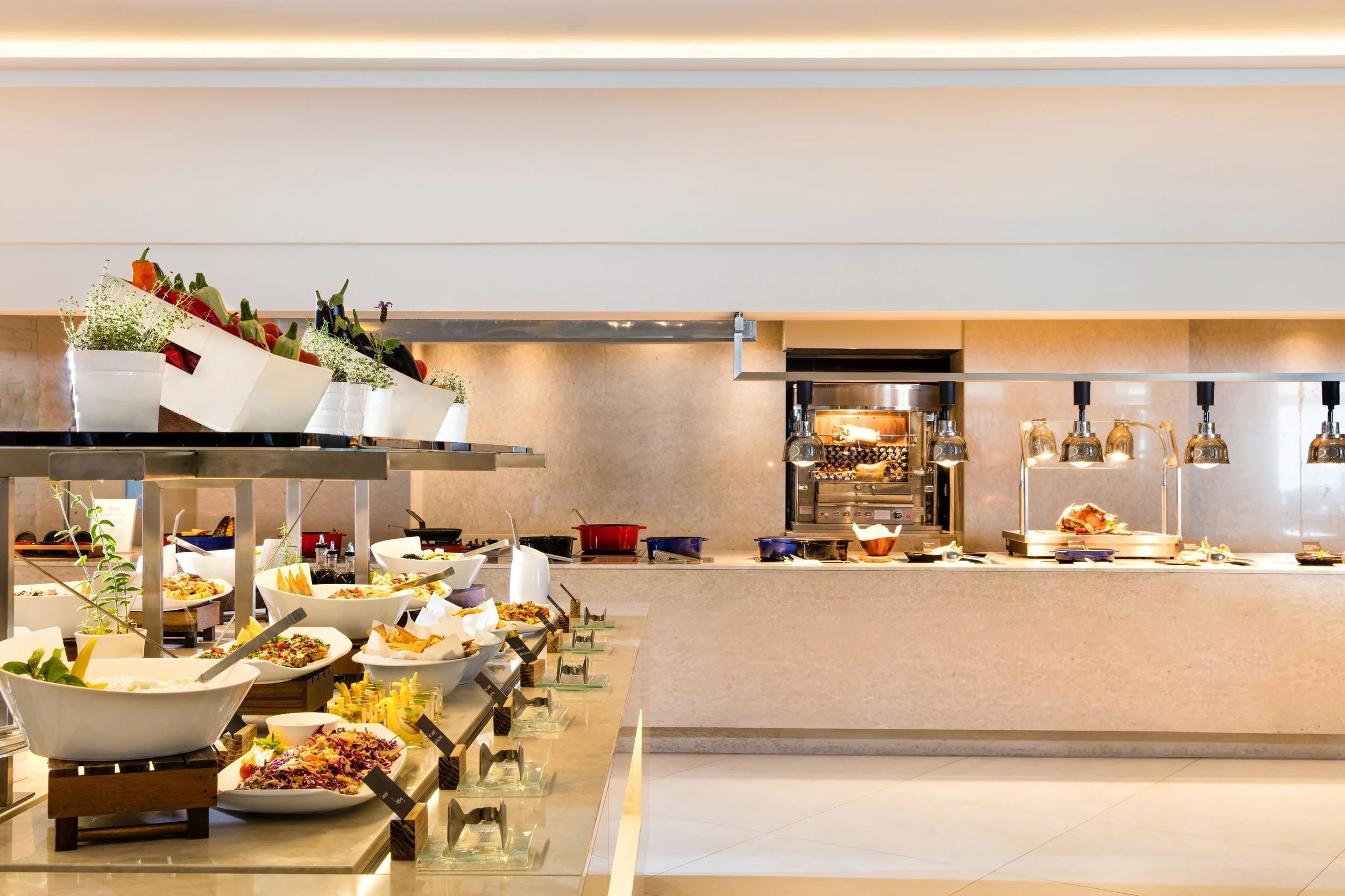 Buffet setup with various salads, dishes, and kitchen equipment in a modern restaurant interior.