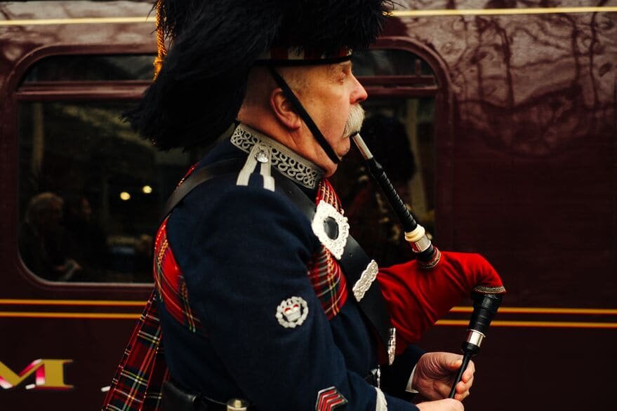 A man dressed in traditional Scottish attire, playing a set of bagpipes.