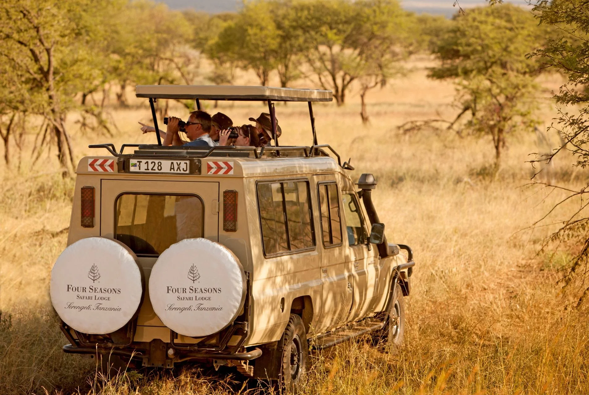 Tourists in a safari vehicle observing wildlife in an open grassland with scattered trees in Serengeti, Tanzania.