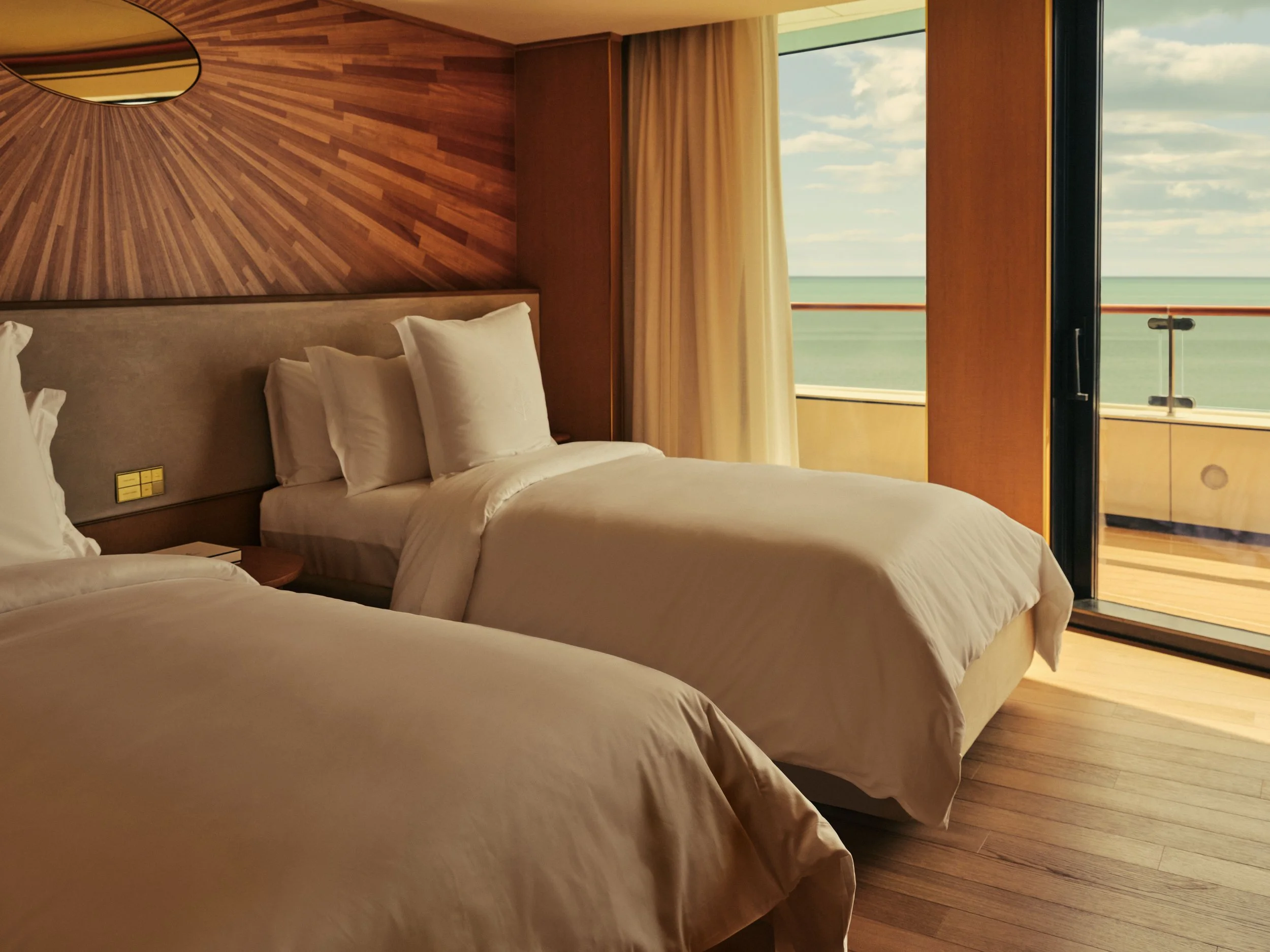 Hotel room with two beds, wooden headboard, and a large window overlooking the ocean and sky.
