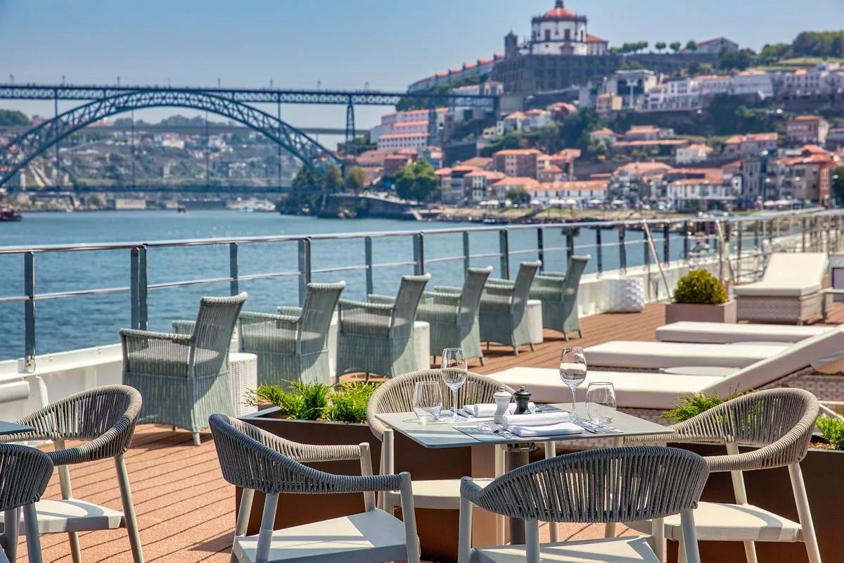 Outdoor dining area on a cruise ship with a view of a river, bridge, and cityscape in Porto, Portugal.