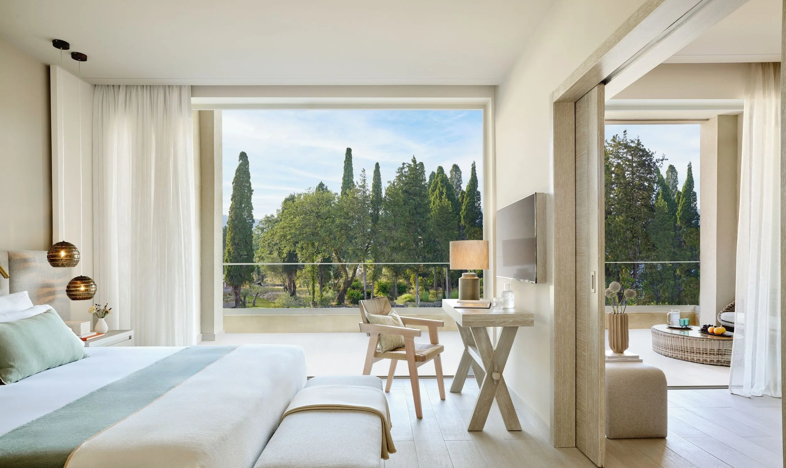 Bright living room with large windows view of trees and sky, modern decor, light-colored furniture, and indoor plants.