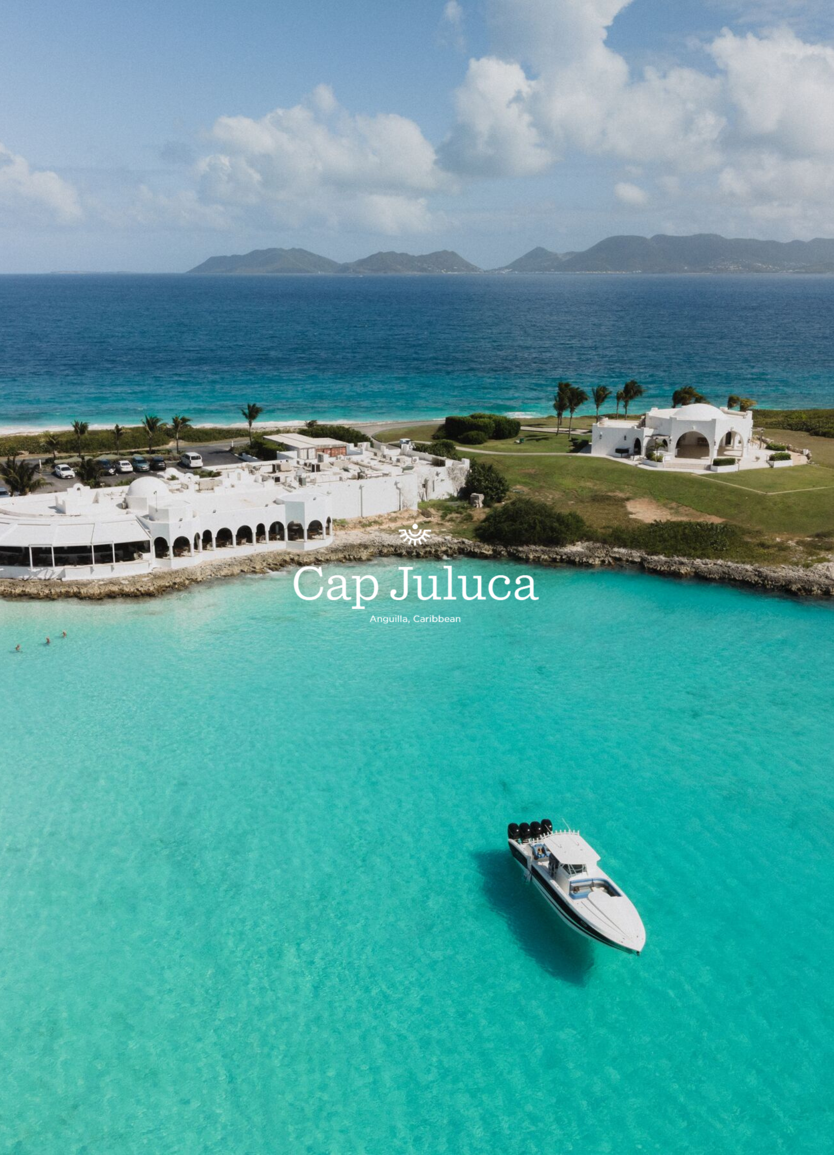 An aerial view of a turquoise bay with a white yacht in the water, and a white building with arches on the shore. There are palm trees, parking lot, and mountains in the background, labeled 'Cap Juluca, Anguilla, Caribbean'.
