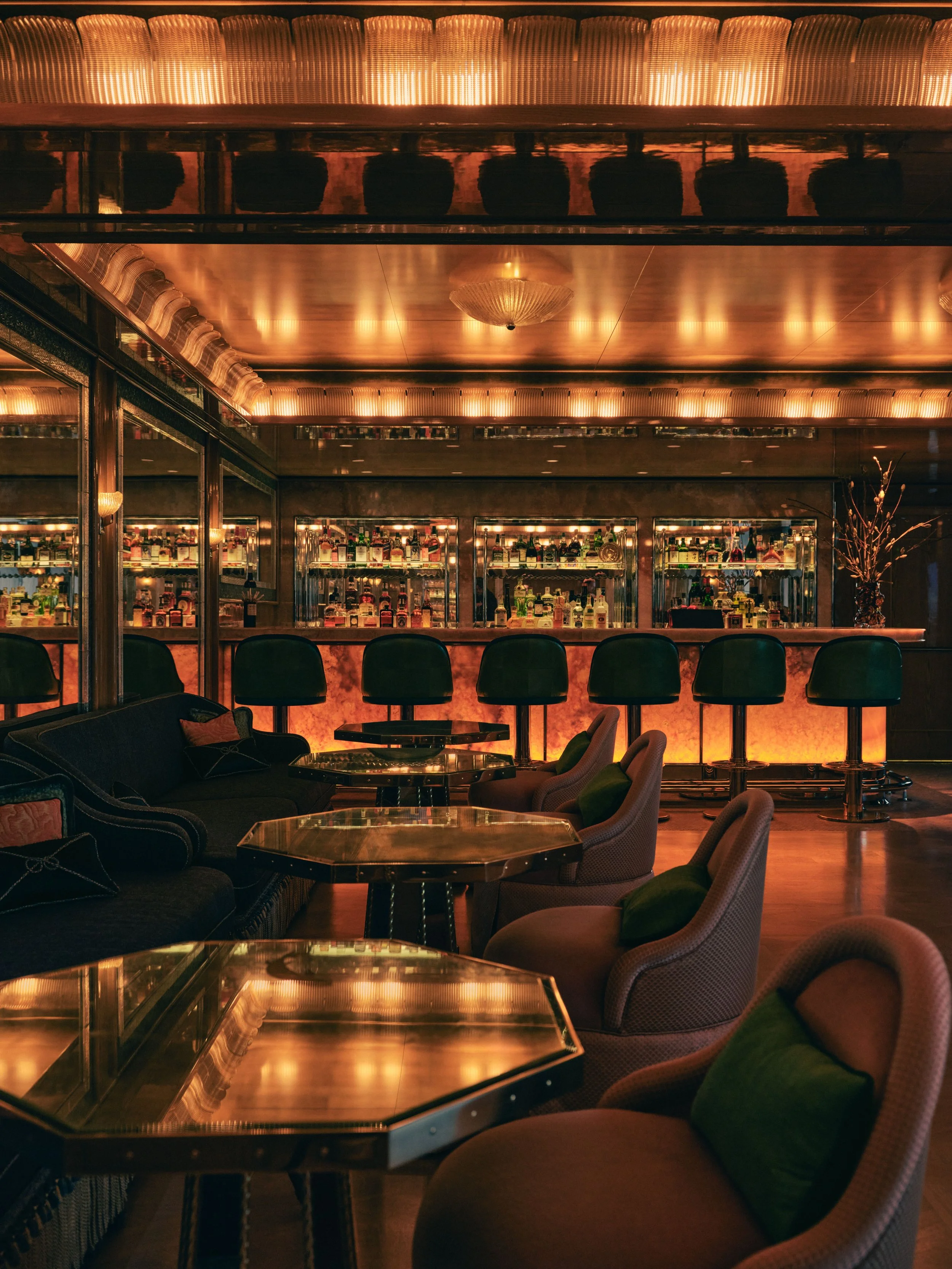 An elegant bar interior with a mirrored back bar displaying various liquor bottles, plush seating, and warm lighting creating a cozy atmosphere.