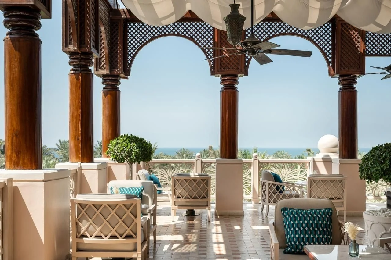 Balcony with white chairs and blue cushions overlooking a scenic view of palm trees and the ocean.