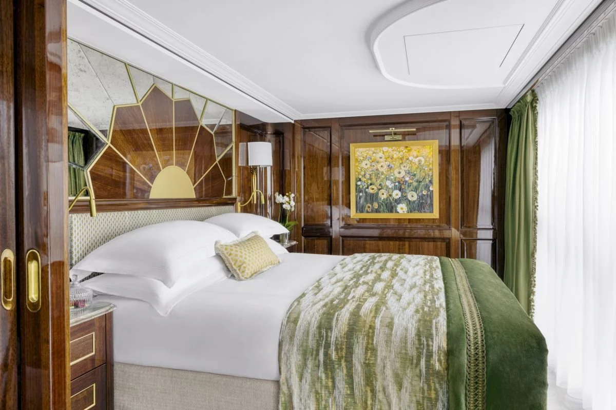 Luxurious hotel bedroom with white bedding, green accents, and wooden paneling. Art featuring sunflowers on the wall and white curtains by a large window.