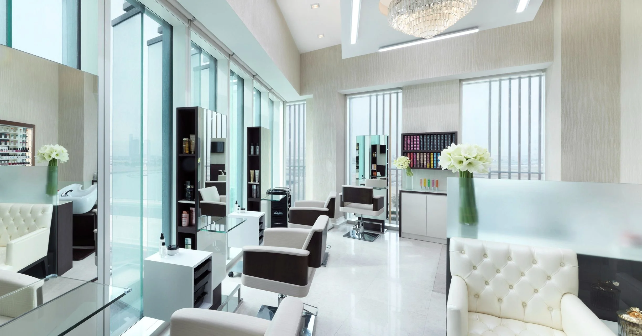 Modern beauty salon interior with chairs, mirrors, and nail polish displays, large windows with city views, and floral decorations.