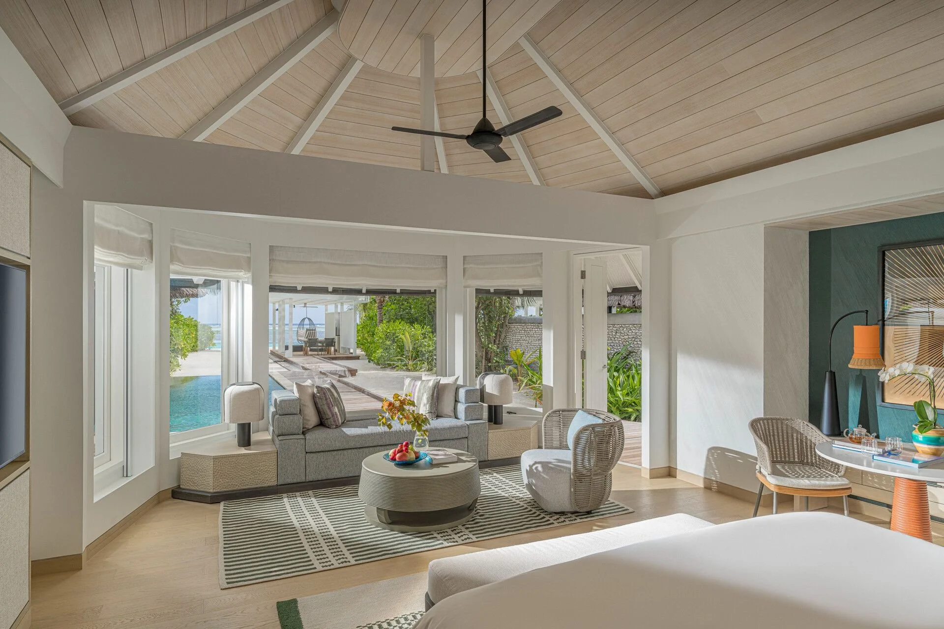 Living room with large windows looking out to an outdoor pool and patio area, ceiling fan, and a mix of modern and coastal decor.