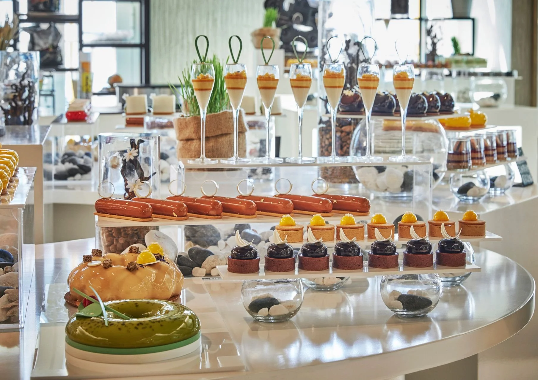 Display of assorted desserts including chocolate, fruit tarts, eclairs, and mousse in a glass showcase at a bakery or cafe.