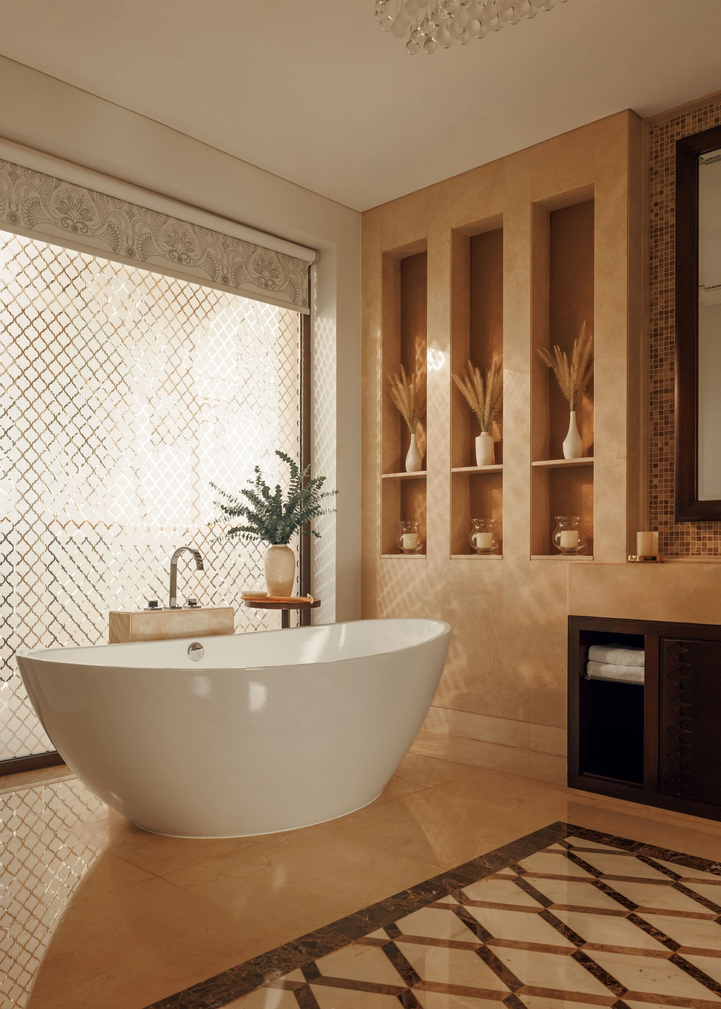 A modern bathroom with a white freestanding bathtub, a large window with patterned blinds, and decorative shelves with vases containing dried plants. The room features beige marble walls and a patterned tile floor.