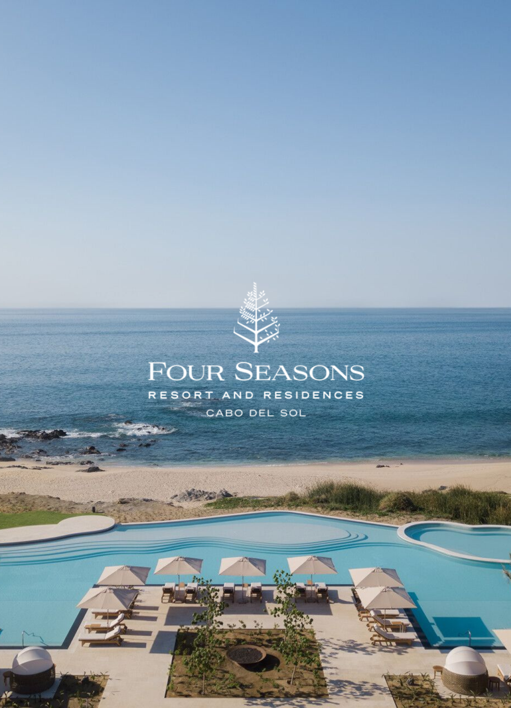 Aerial view of a resort with a large swimming pool, surrounded by lounge chairs with umbrellas, a landscaped garden, and the ocean in the background, at Four Seasons Resort and Residences in Cabo San Lucas.