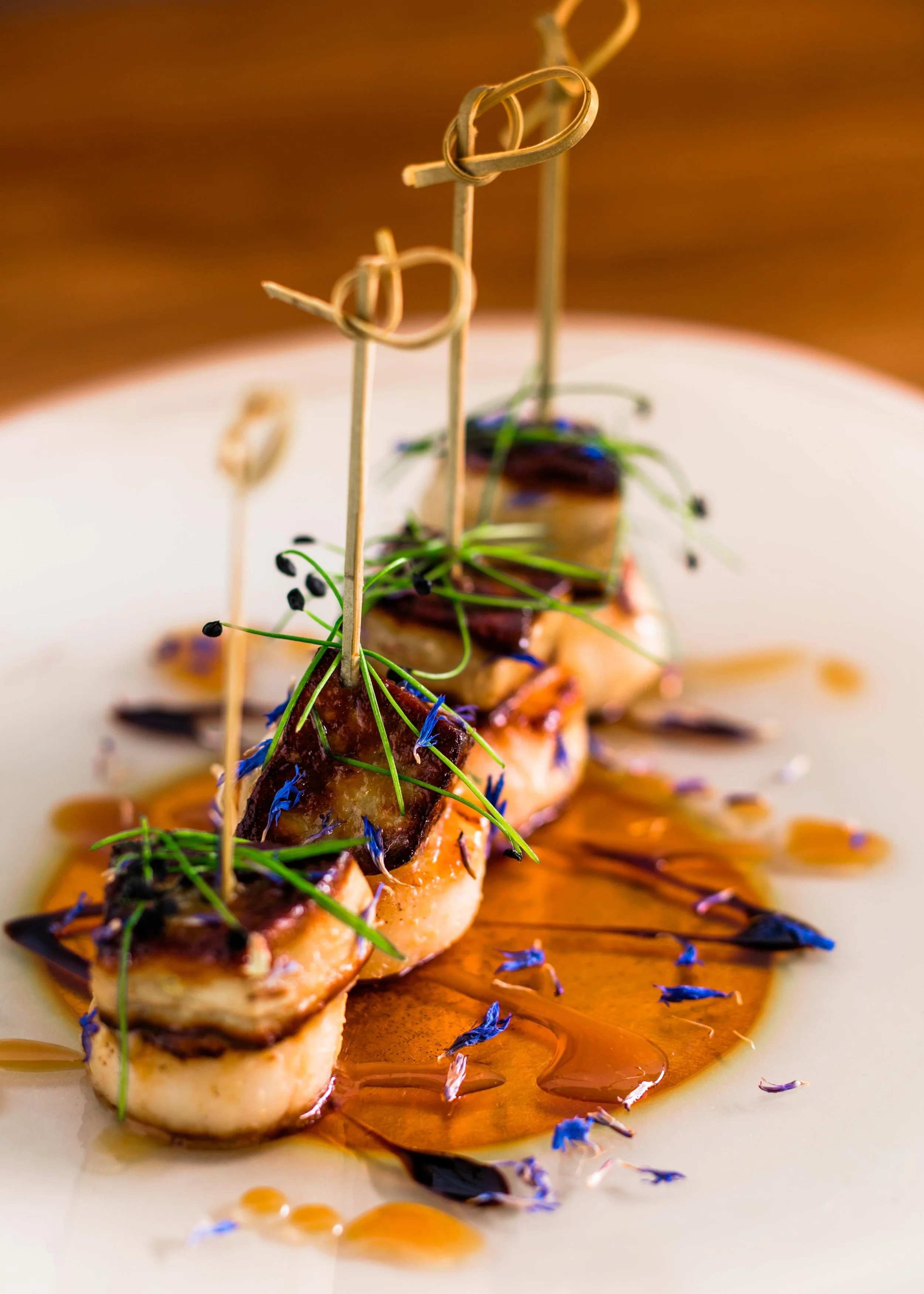 Close-up of a gourmet dish featuring a piece of fish topped with herbs and edible flowers, drizzled with sauce, on a white plate.