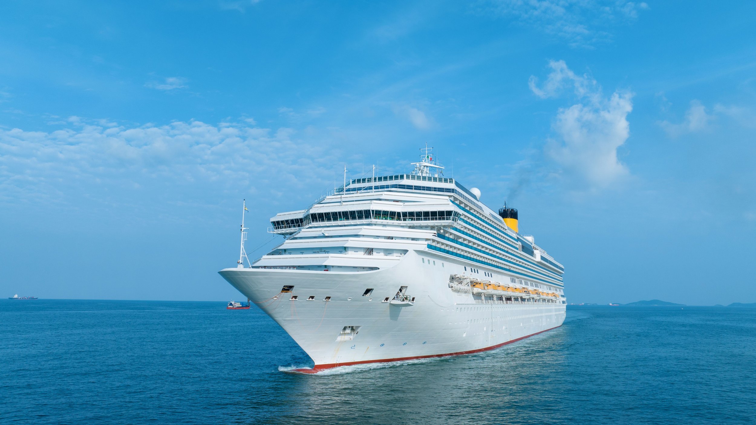 Large white cruise ship sailing on calm blue ocean waters under a partly cloudy sky.