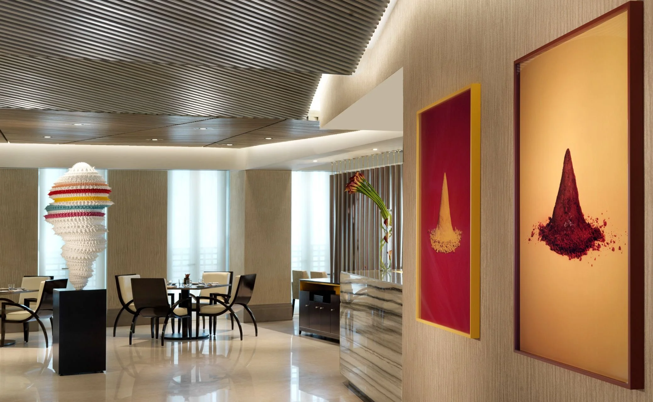 Interior of a modern dining area with artwork on the walls, a sculptural lamp, and a table set with chairs.