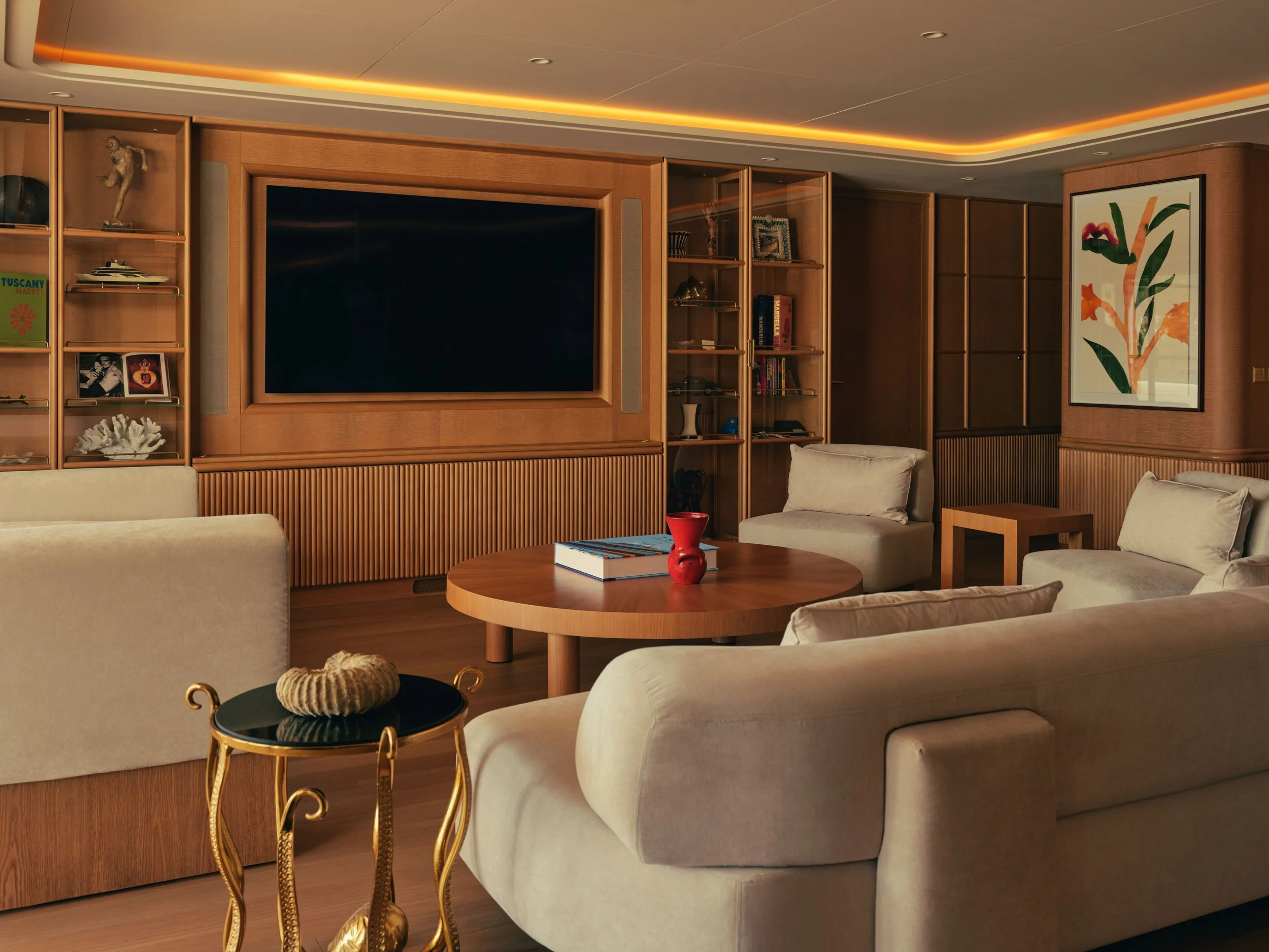 Living room with beige sofa, wooden shelves, a large flat-screen TV, contemporary artwork, and a vase on a side table.