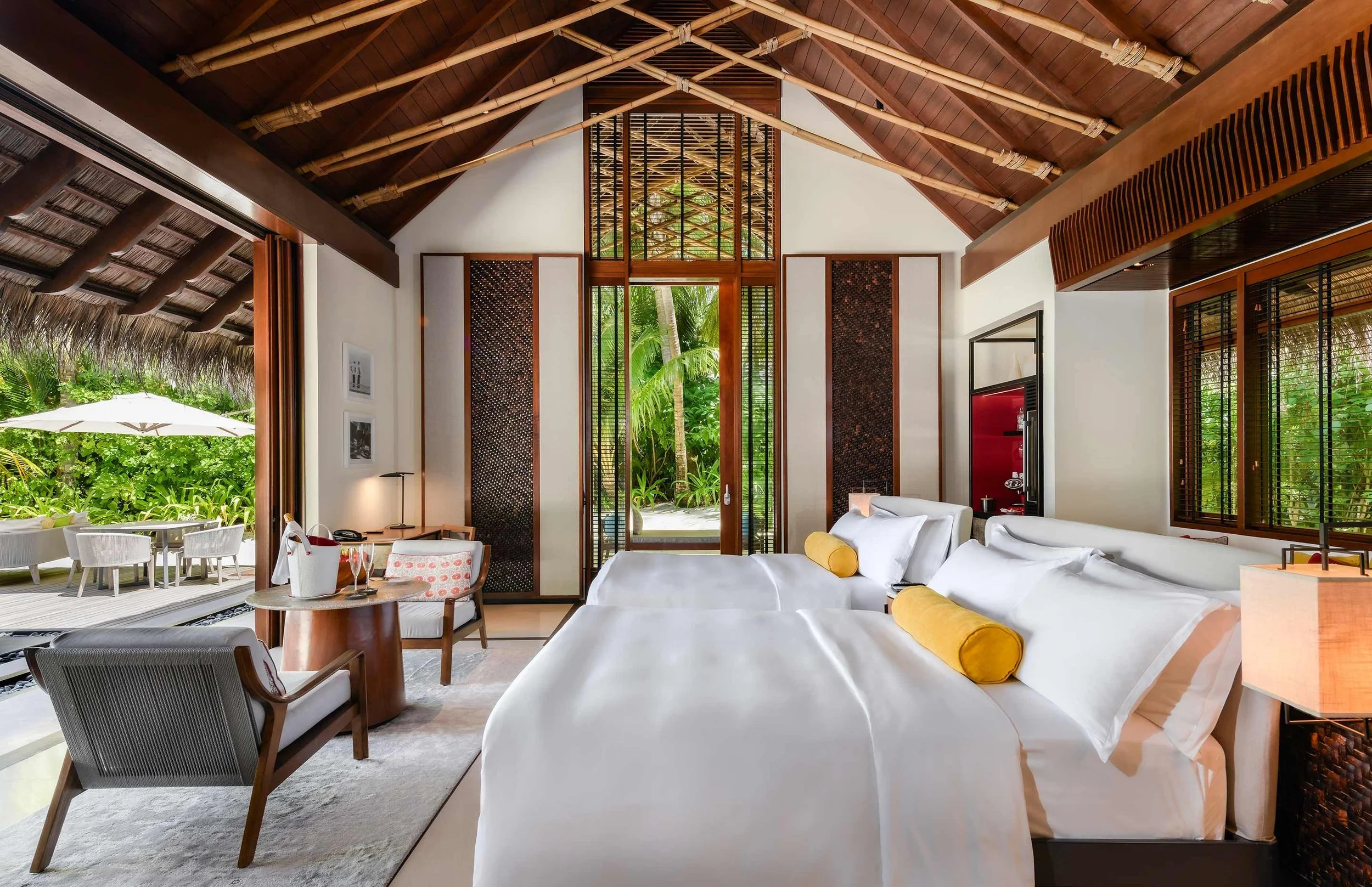 Contemporary hotel room with white beds, wood accents, and large windows opening to a lush tropical garden with palm trees.