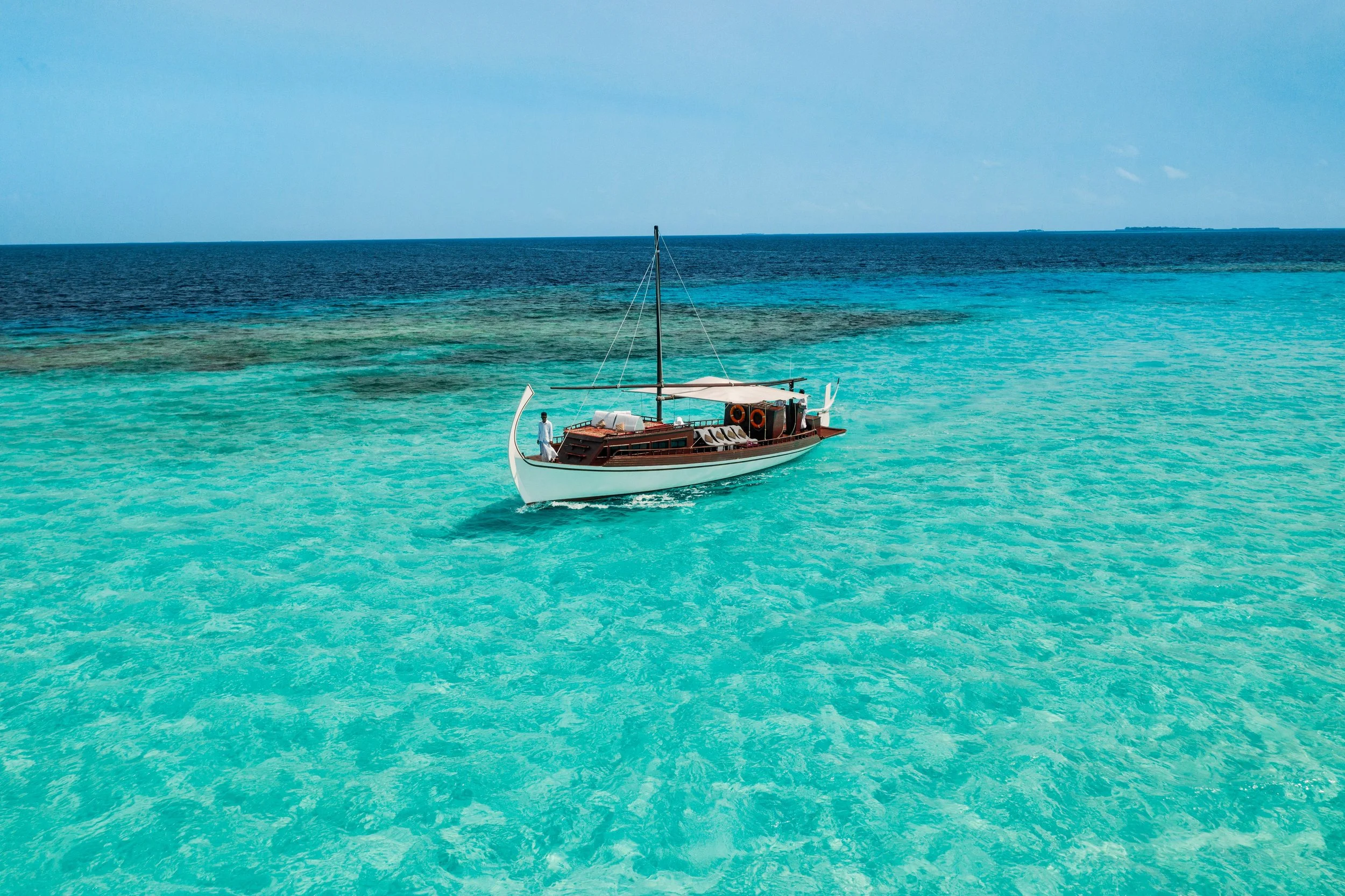 A sailboat on clear turquoise water with a distant horizon and an island in the background.