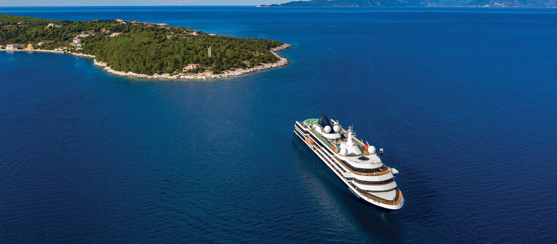 Large cruise ship sailing in calm blue water near a lush green island.