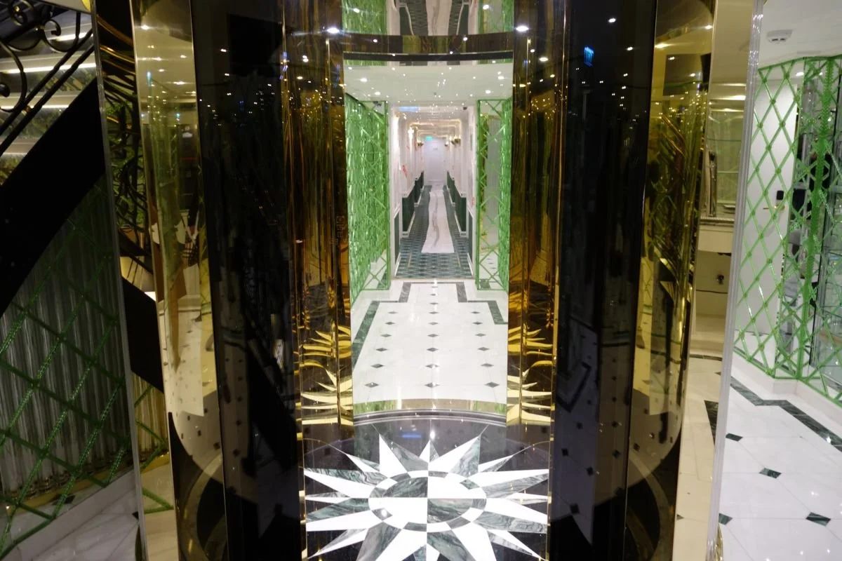 Elegant hotel lobby with marble flooring, gold accents, and green lattice wall patterns, leading to a hallway in the distance.