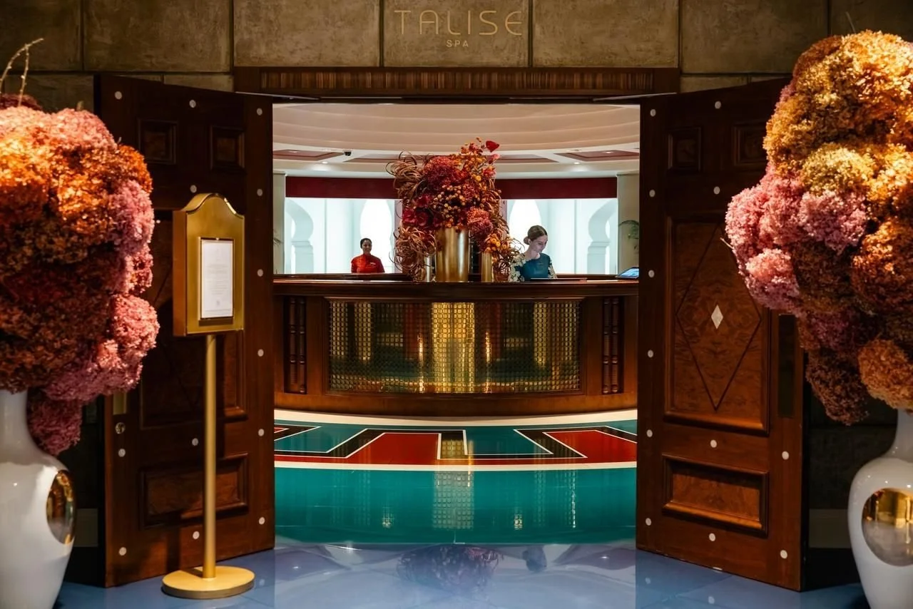 View of hotel reception area at Talise Spa, with large floral arrangements on either side of open wooden doors leading to a check-in counter and guests in the background.
