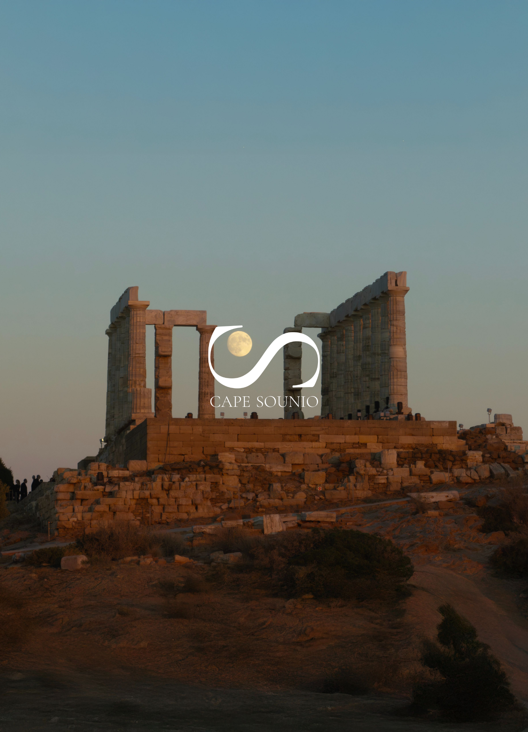 Ancient ruins of columns on a hill at dusk with the full moon in the sky, and a few people walking nearby. The sky transitions from light to darker shades as night falls.